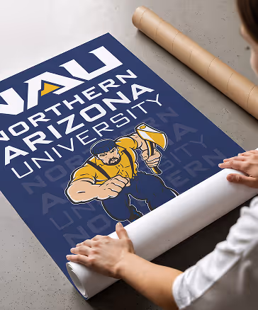 Hands unrolling a navy Northern Arizona University poster featuring the gold Lumberjack mascot and repeated university wordmarks.