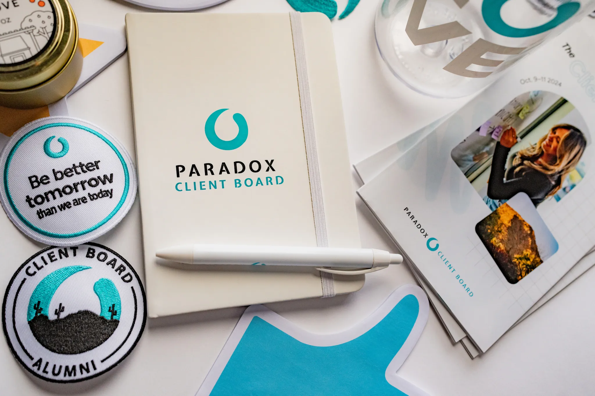 Paradox Client Board branded notebook, pen, patches, flyers, and other promotional items on a white surface.