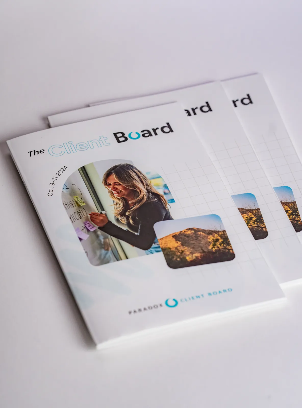 A stack of printed "The Client Board" event programs, the cover showing an attendee at a workshop.