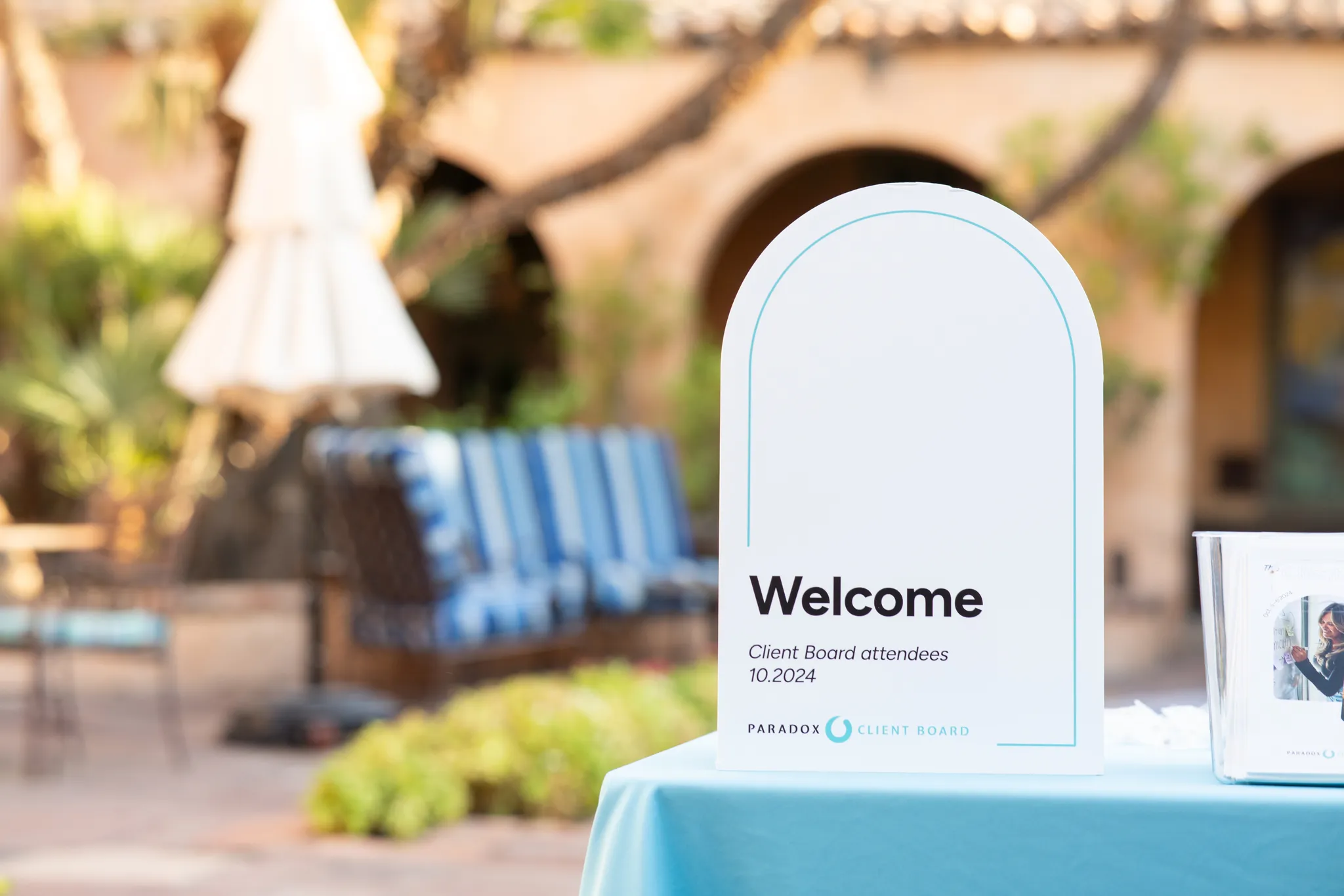 Welcome sign for Paradox Client Board attendees on a blue tablecloth at outdoor venue.