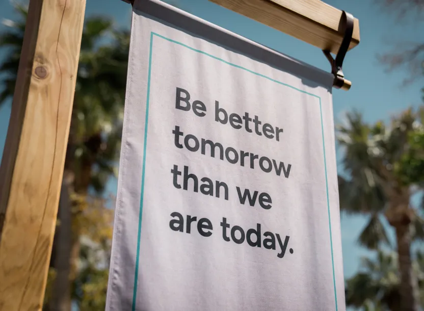 Outdoor fabric banner on wooden frame with motivational text: Be better tomorrow than we are today.