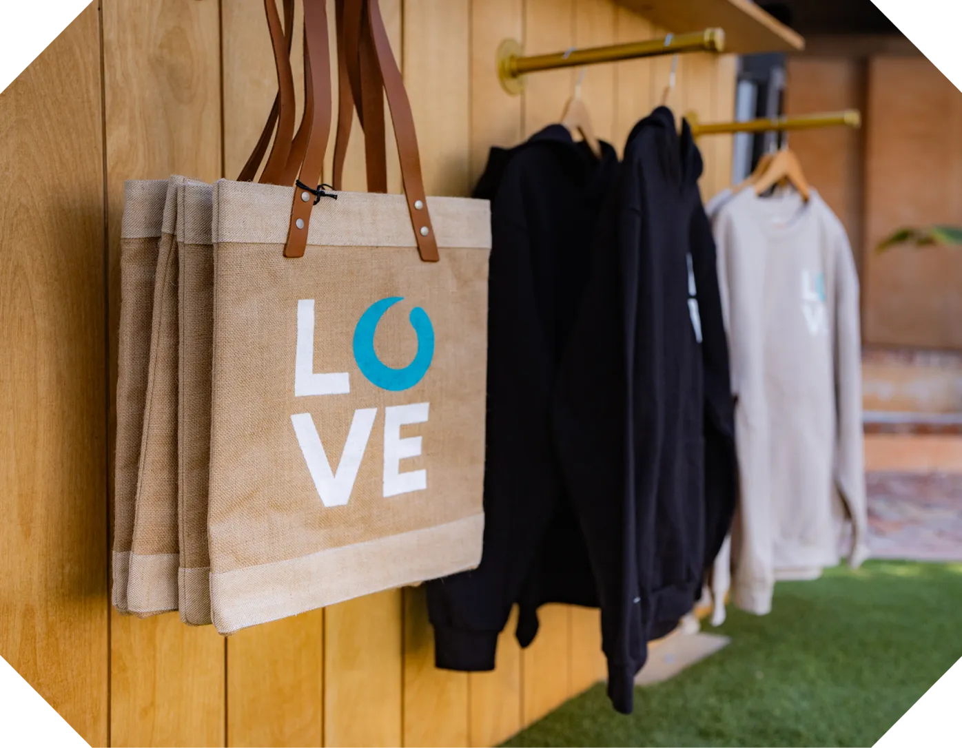 Beige tote bags with LOVE text and black and white hoodies hanging on a wood wall rack.