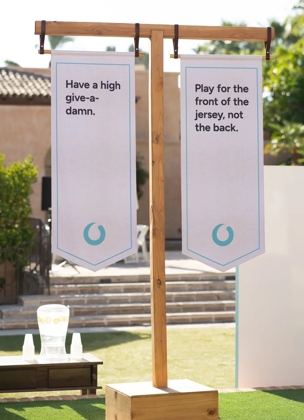 Two vertical banners on wooden stand with motivational texts outdoors near a building.