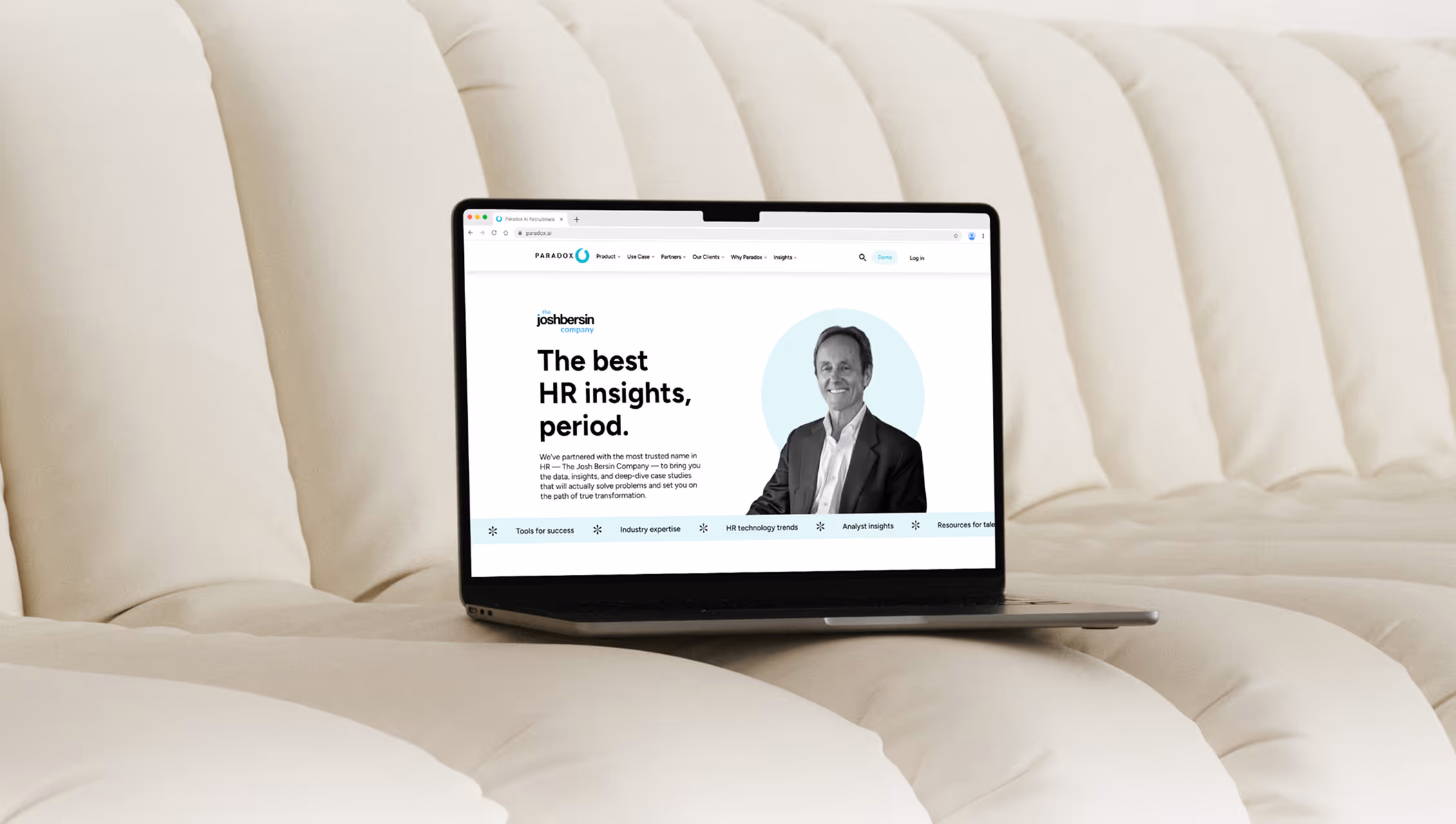 A laptop resting on a cream sofa, displaying a Paradox page headlined "The best HR insights, period." beside a portrait photograph.