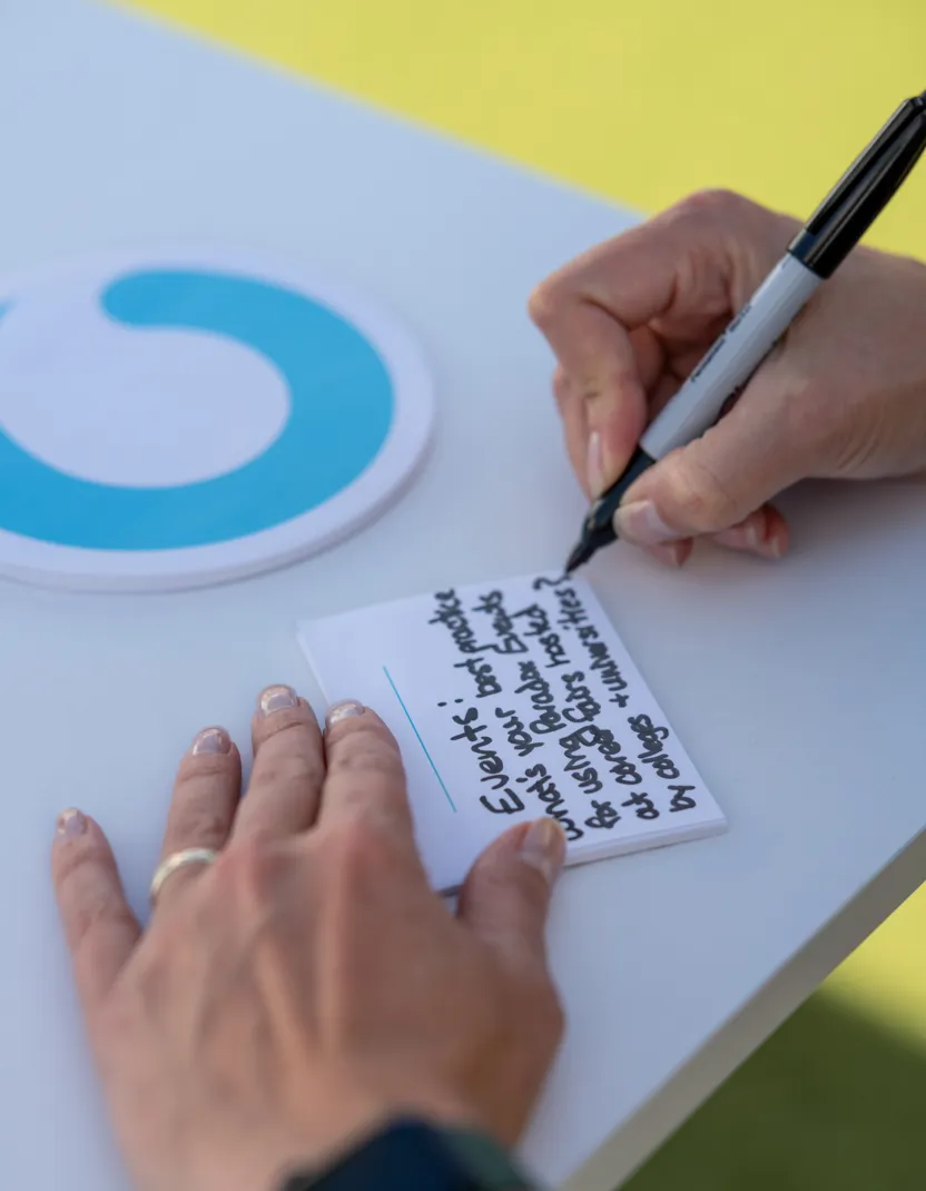 Person writing notes on a small paper pad with a black marker on a white table.