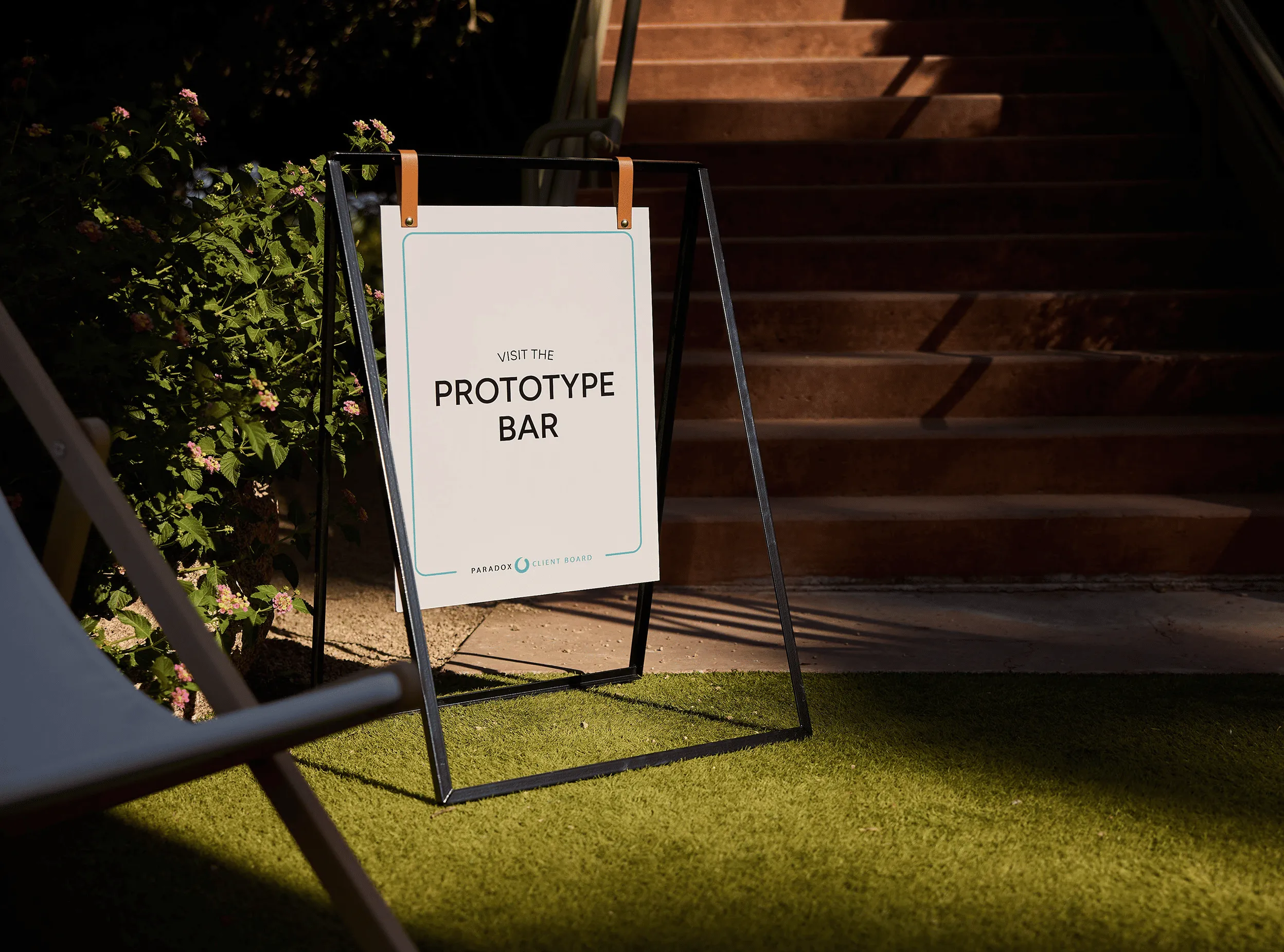 Sign on grass by stairs reading 'Visit the Prototype Bar' with plants in the background.