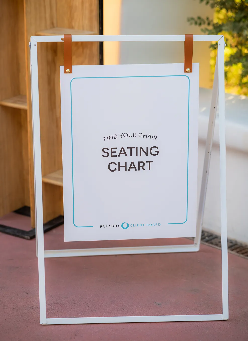 White sign on stand with text 'Find your chair Seating Chart' outside on a patio.