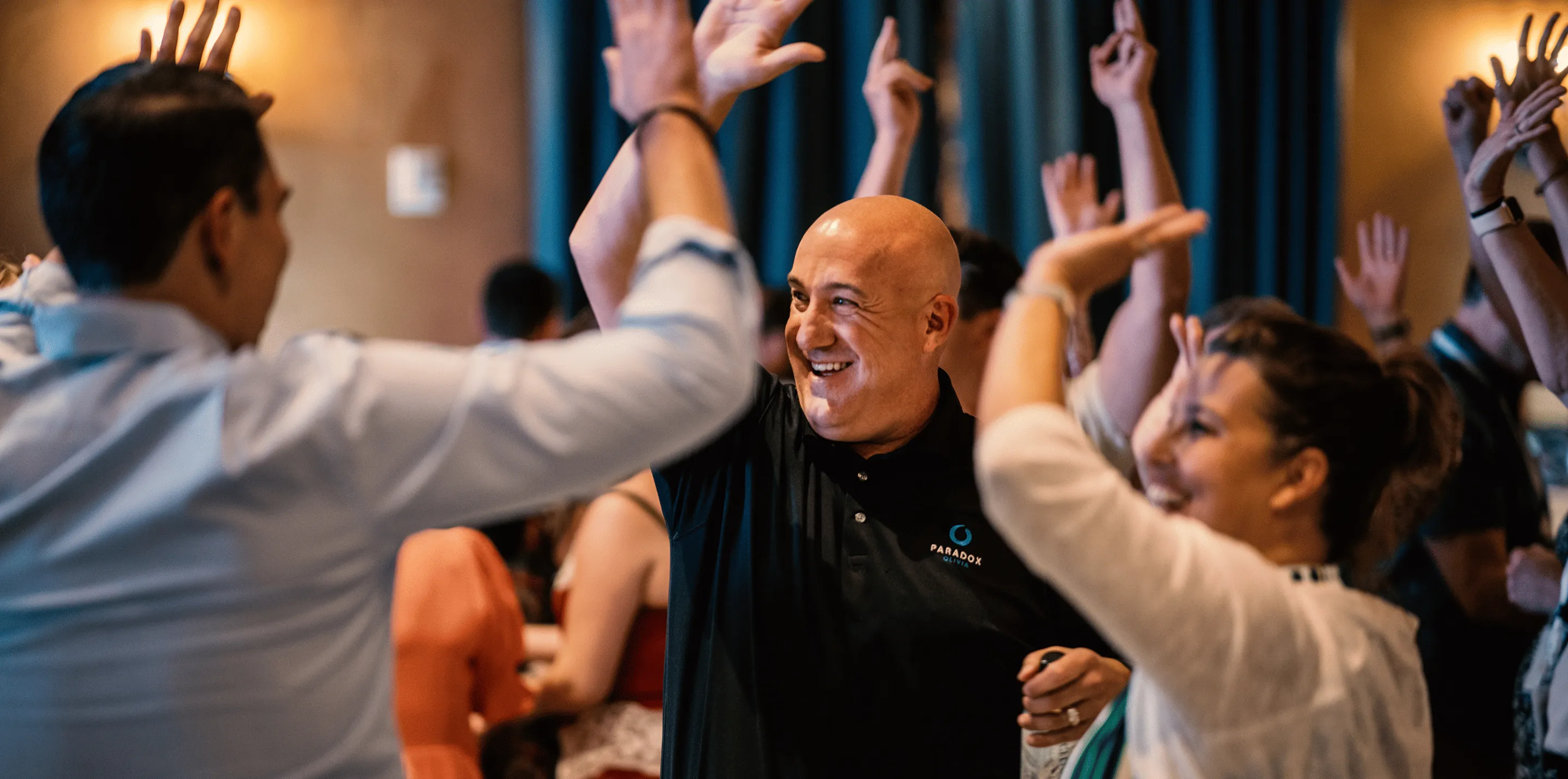 Smiling people enthusiastically raise hands for a group high-five in a lively indoor setting.