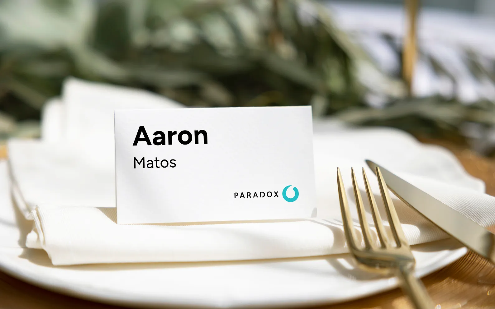 Table setting with a white napkin, fork, knife, and a name card reading Aaron Matos, Paradox logo.