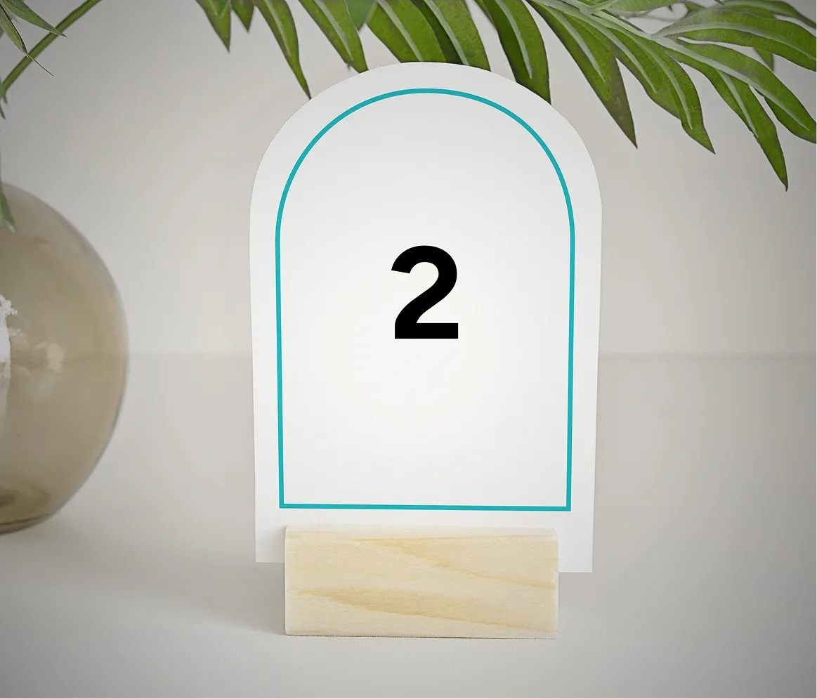 Table number 2 card in a wooden holder with green leaves overhead and a glass vase on the side.
