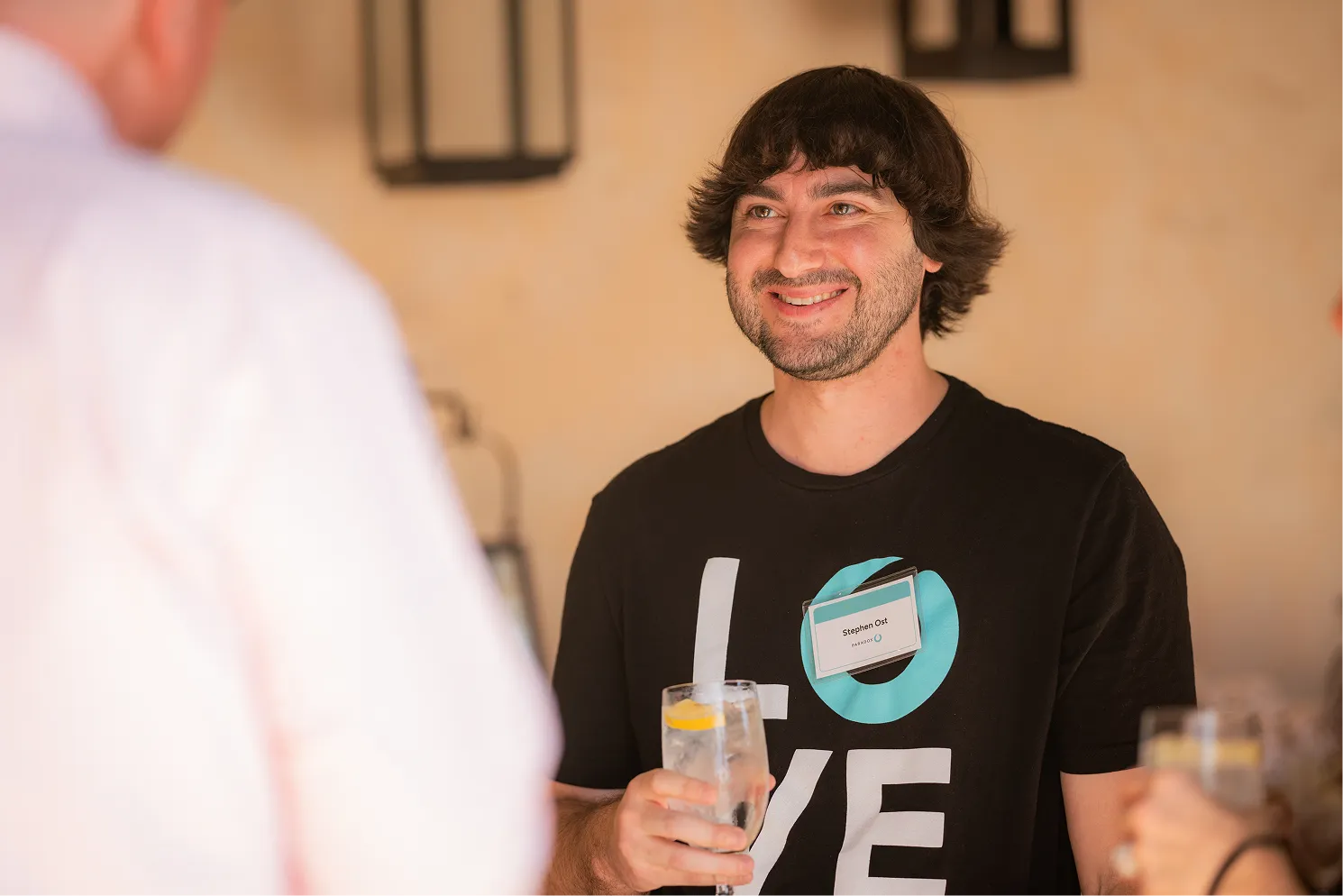 Smiling man in black LOVE shirt with name tag holding a glass of water with lemon.