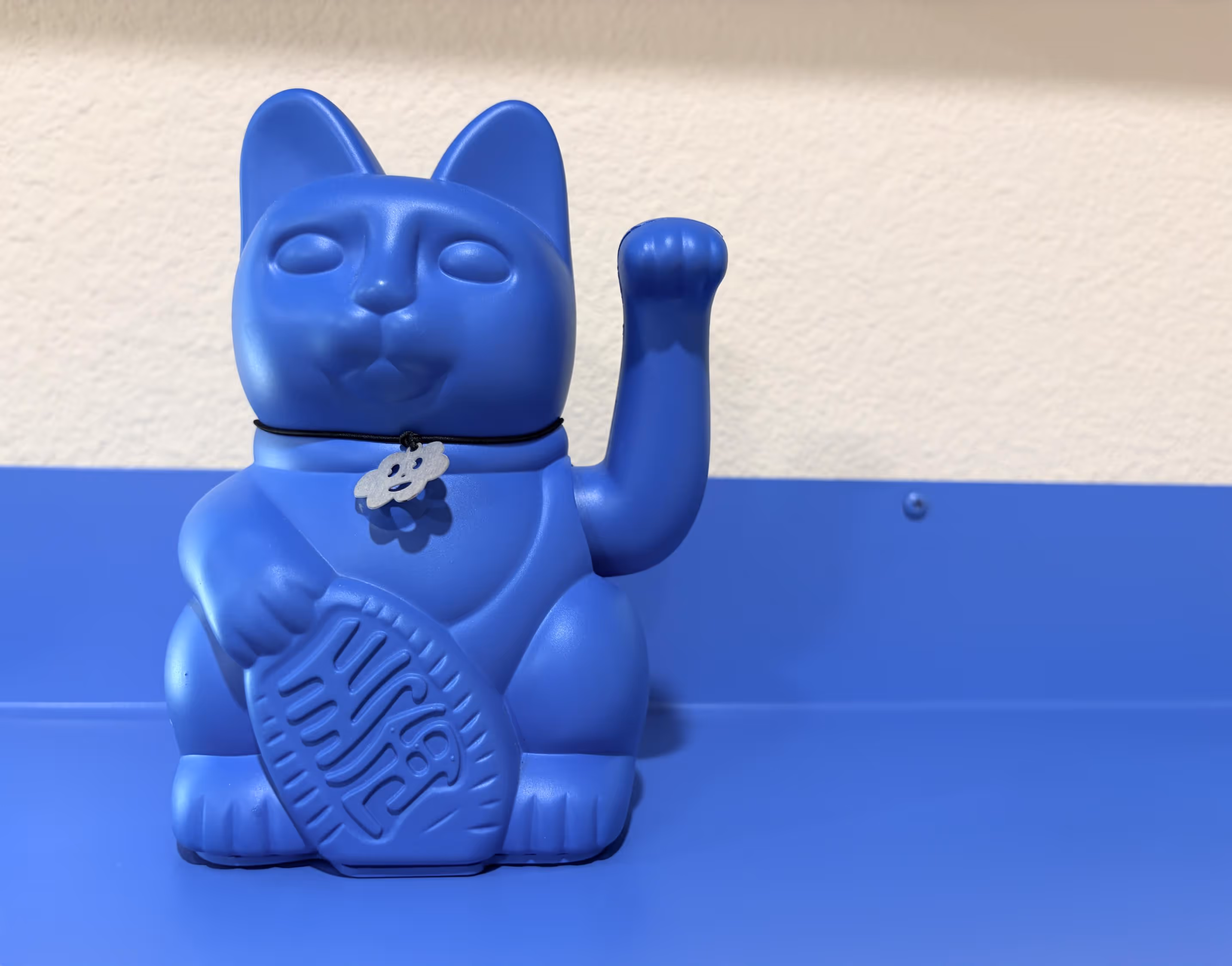 A blue maneki-neko beckoning cat figurine against a blue and cream wall.