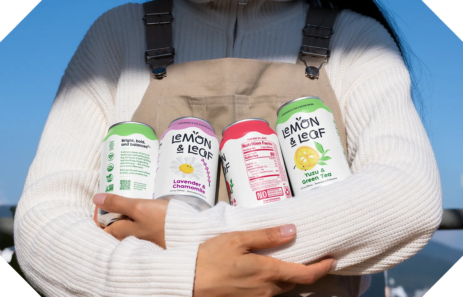 A person holding an armful of Lemon & Leaf cans against their chest.