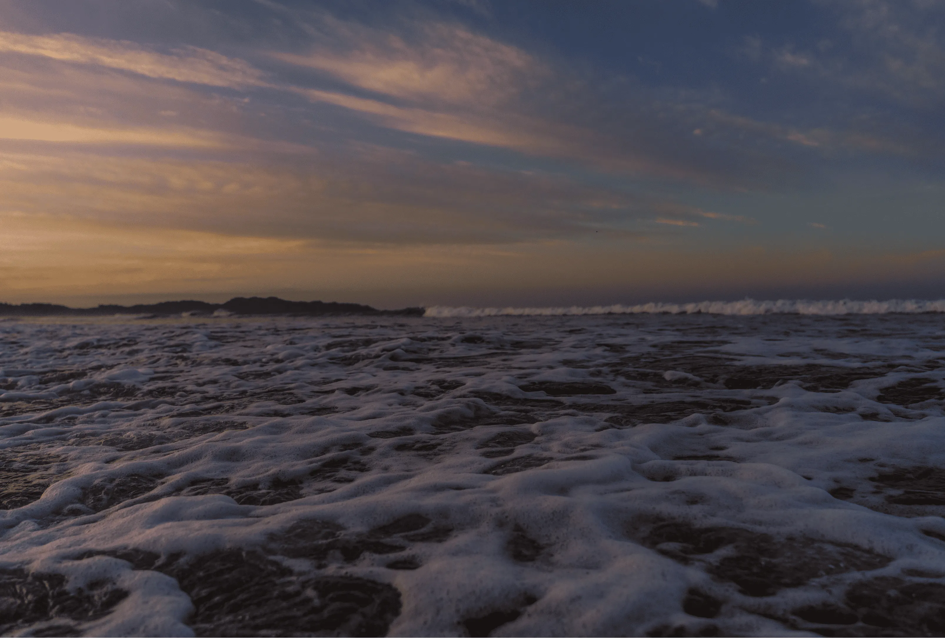 A coastal sunset with waves washing over rocks.