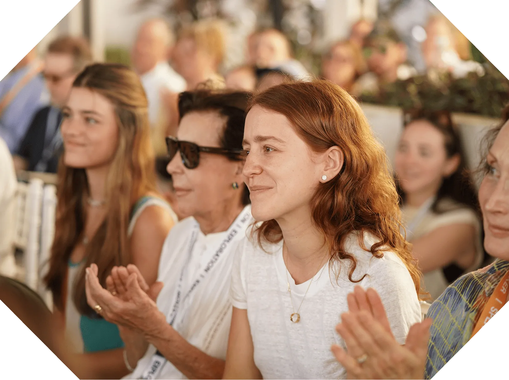 Audience of diverse women clapping and smiling attentively at an event or presentation.