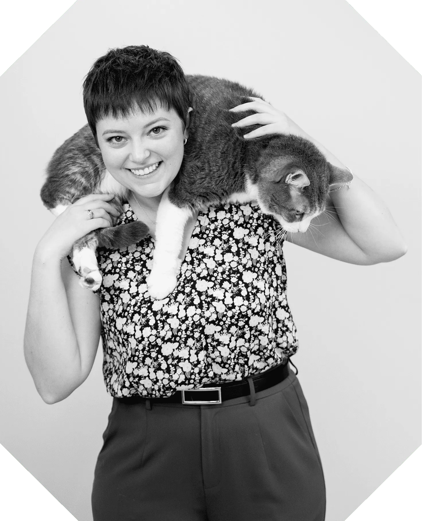 A black and white photograph of Maddie Moe laughing with a grey and white cat draped across her shoulders.