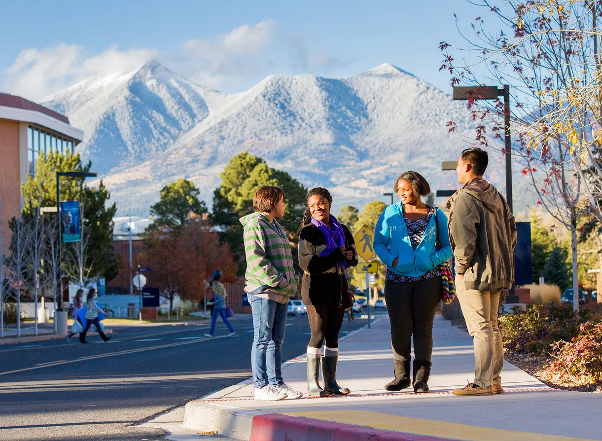 Students standing together on campus with snow-capped mountains behind them.
