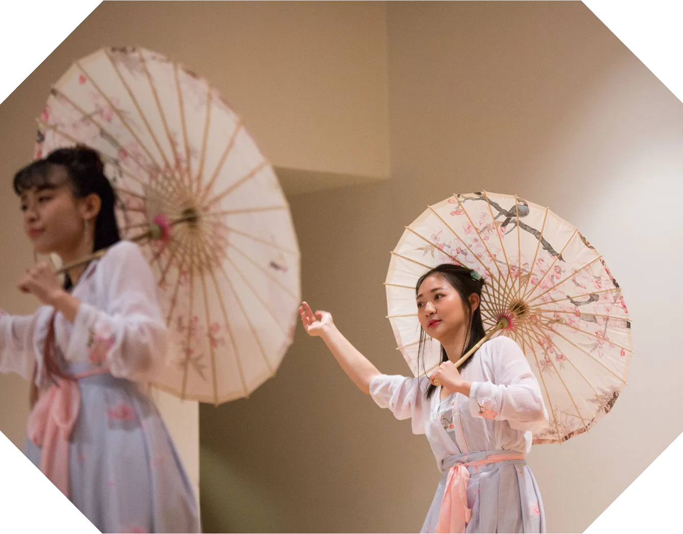 Two performers in traditional dress holding painted parasols at a cultural event.