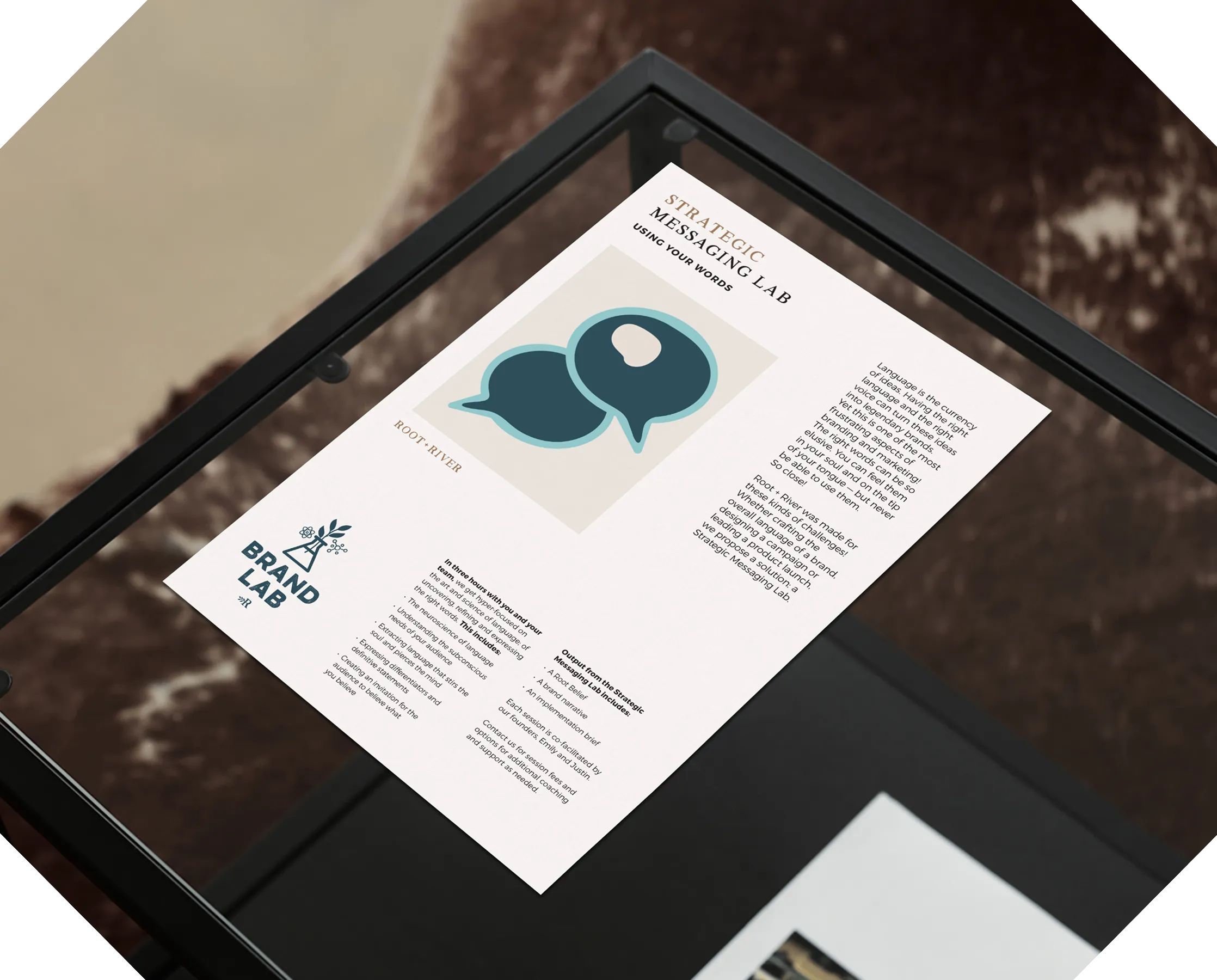 A printed Root + River one-sheet on a glass table, headed with a speech-bubble mark.
