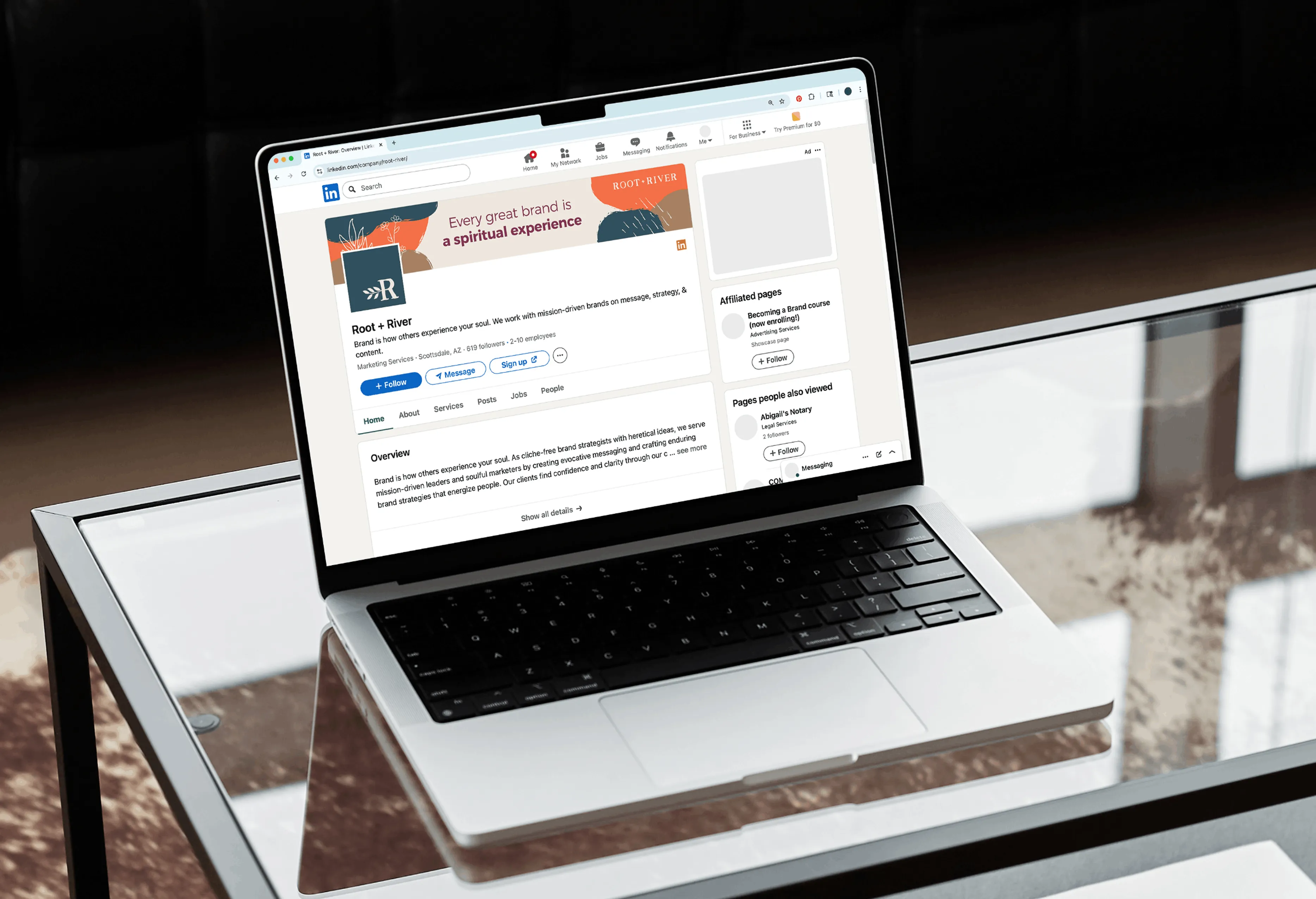 A laptop on a glass table displaying a Root + River article page.