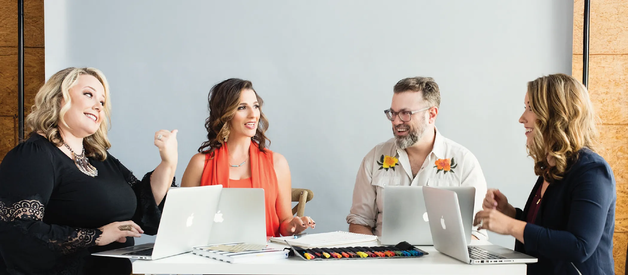 Four people talking around a table with laptops in a bright room.