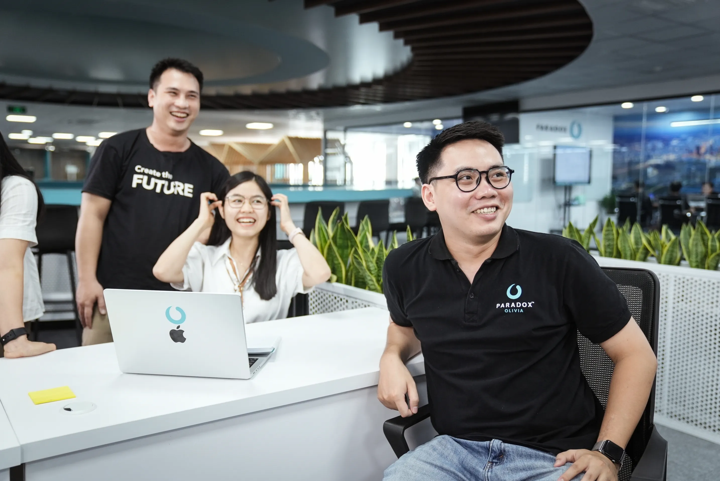 Two Paradox employees in branded t-shirts working together at a laptop in a bright modern office.