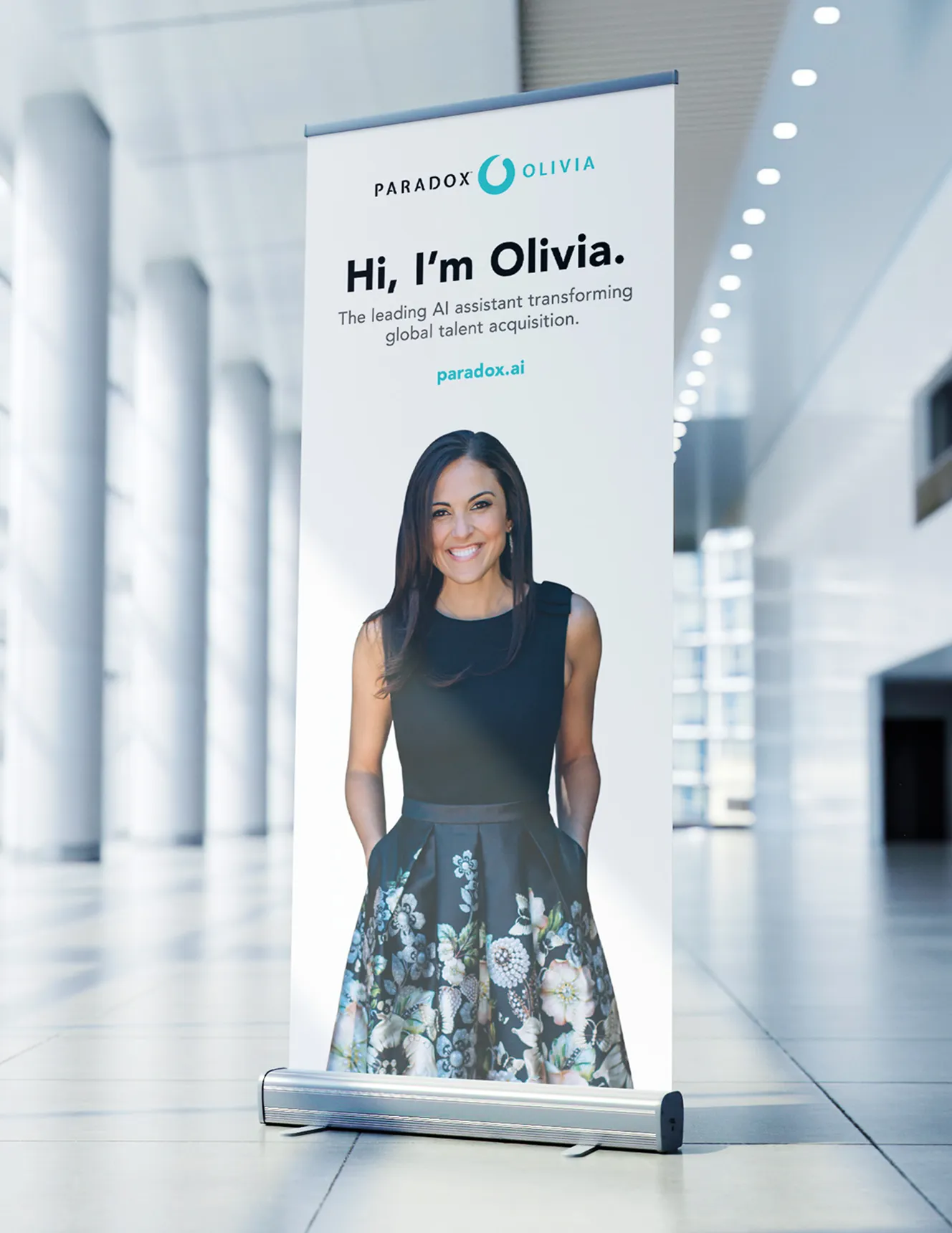 A Paradox pull-up banner in an office lobby reading "Hi, I'm Olivia." with a full-length photograph.