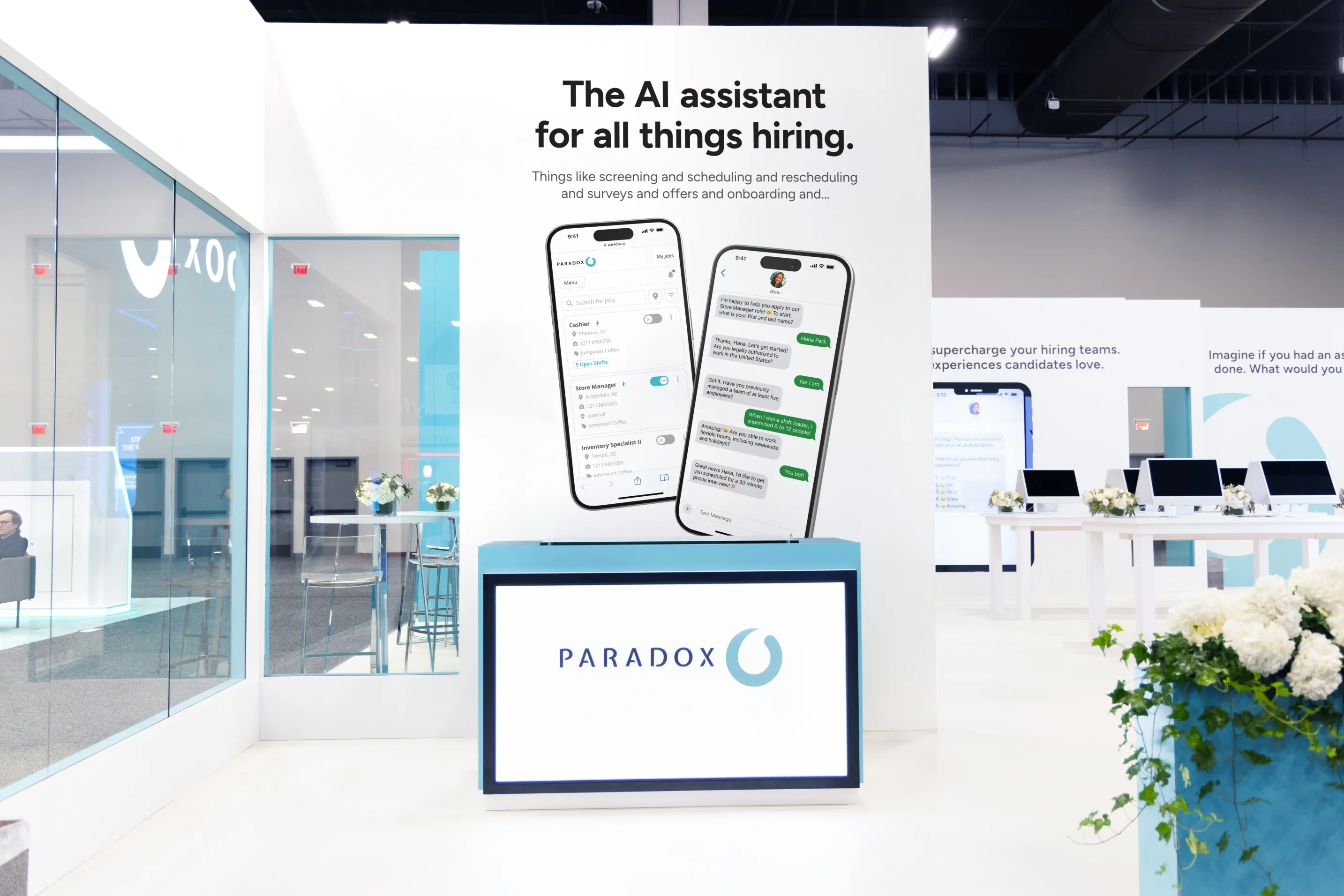 A Paradox booth panel reading "The AI assistant for all things hiring." beside a large phone display.