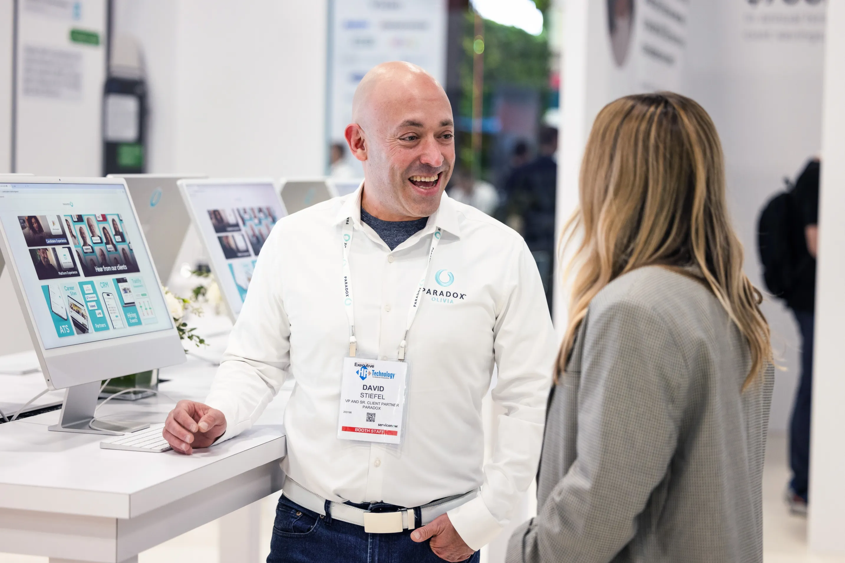 A Paradox team member in conversation with an attendee beside demo screens.