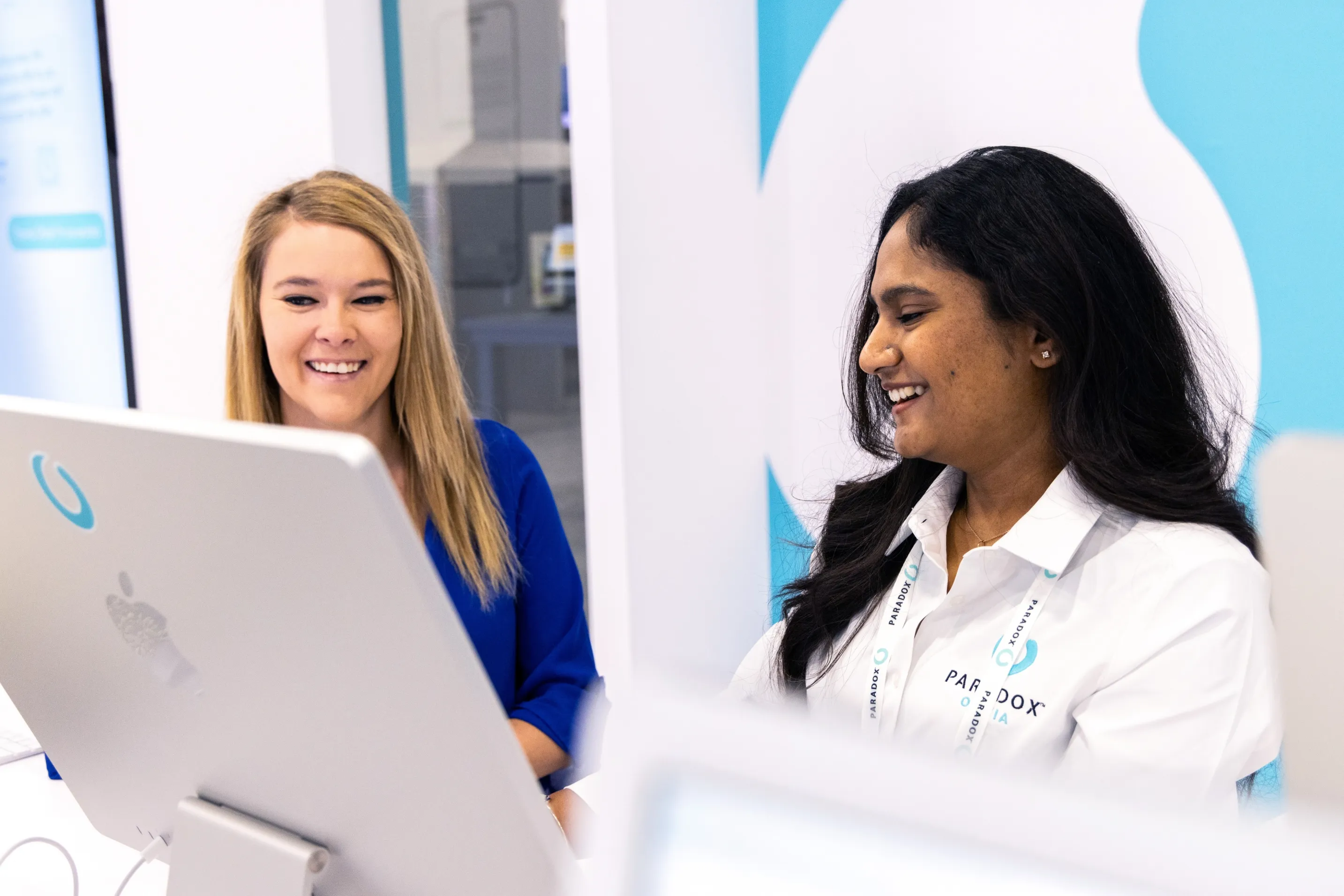 Two Paradox team members smiling behind a demo monitor at a conference stand.