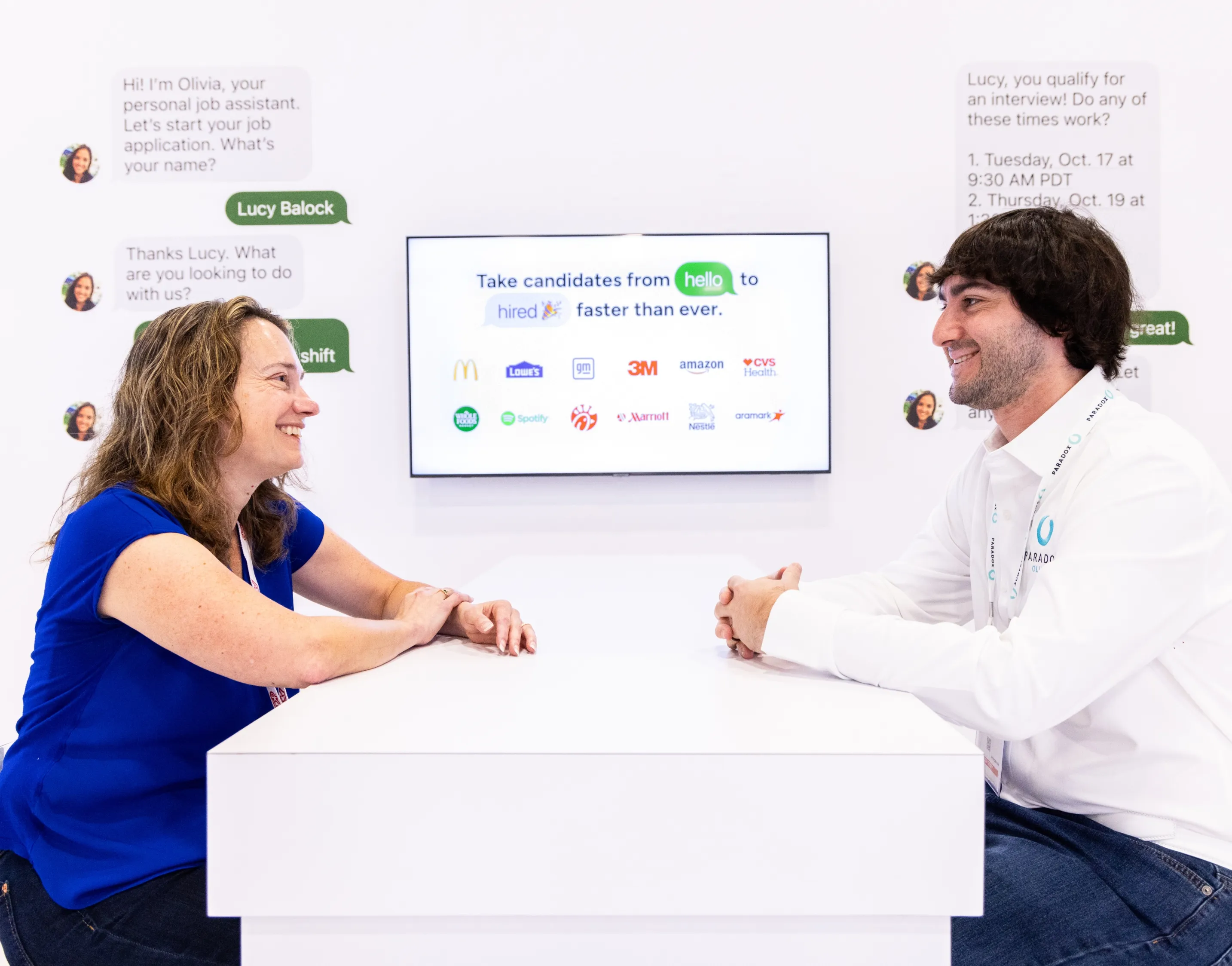 Two people talking across a white counter in front of a Paradox candidate conversation screen.
