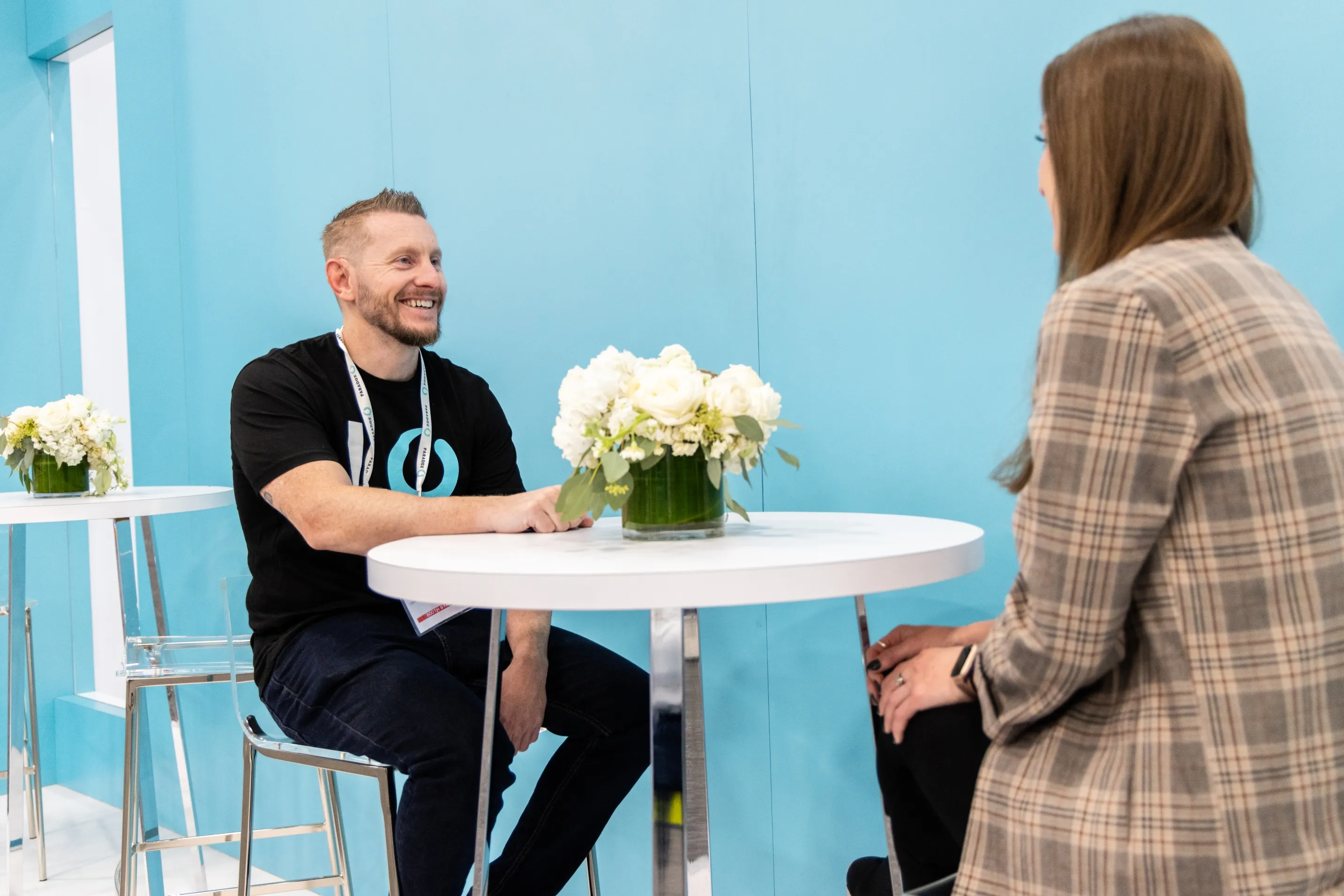 Two people talking across a small round table at a Paradox event stand.