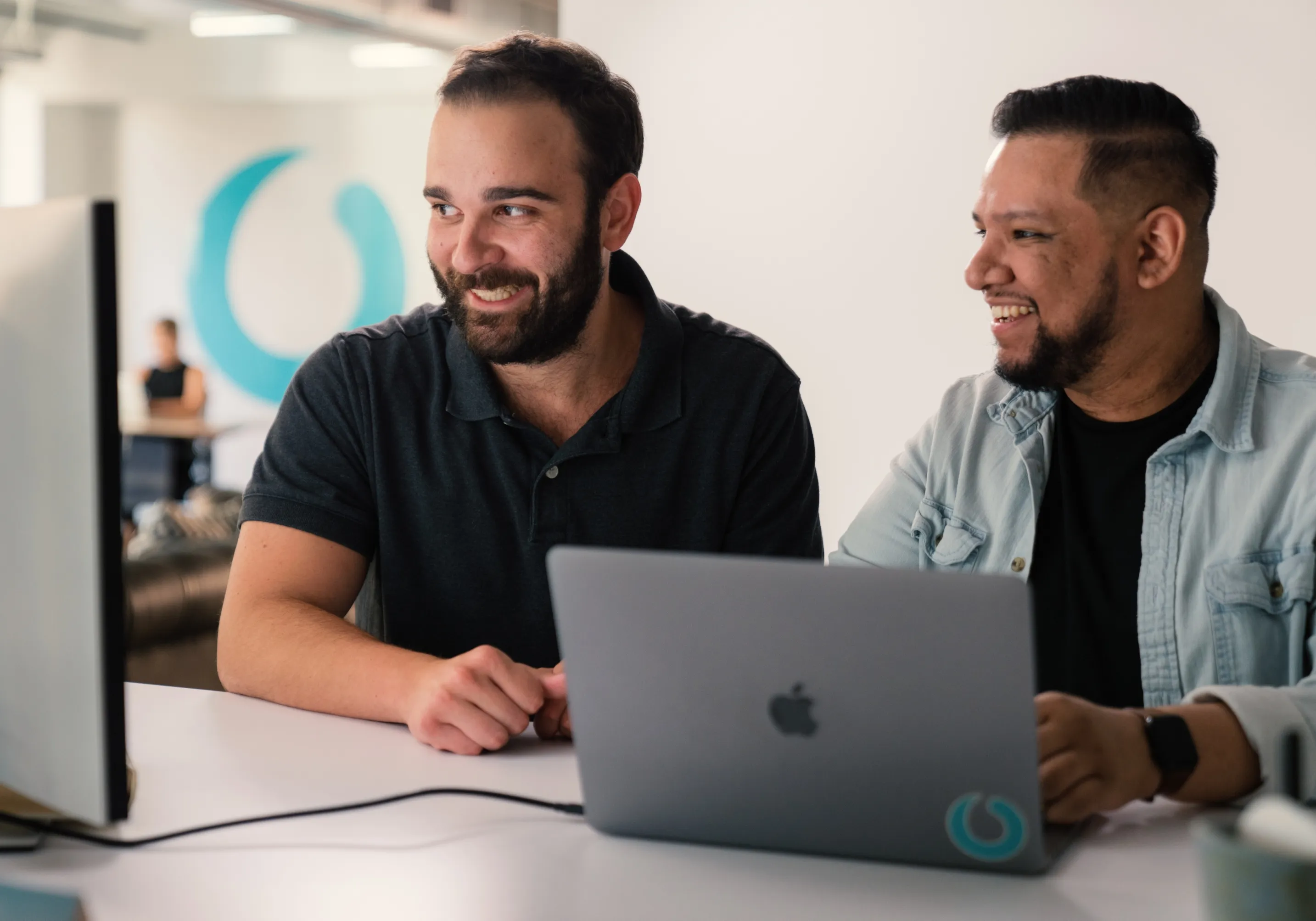 Two colleagues laughing at a laptop in a Paradox office, the brand mark on the wall behind them.