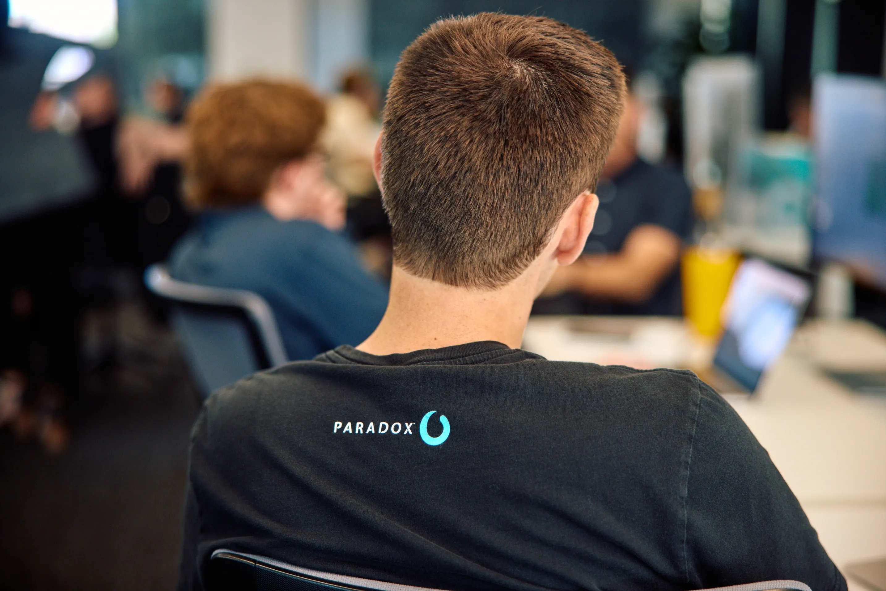 A man seen from behind wearing a black Paradox t-shirt at a company event.