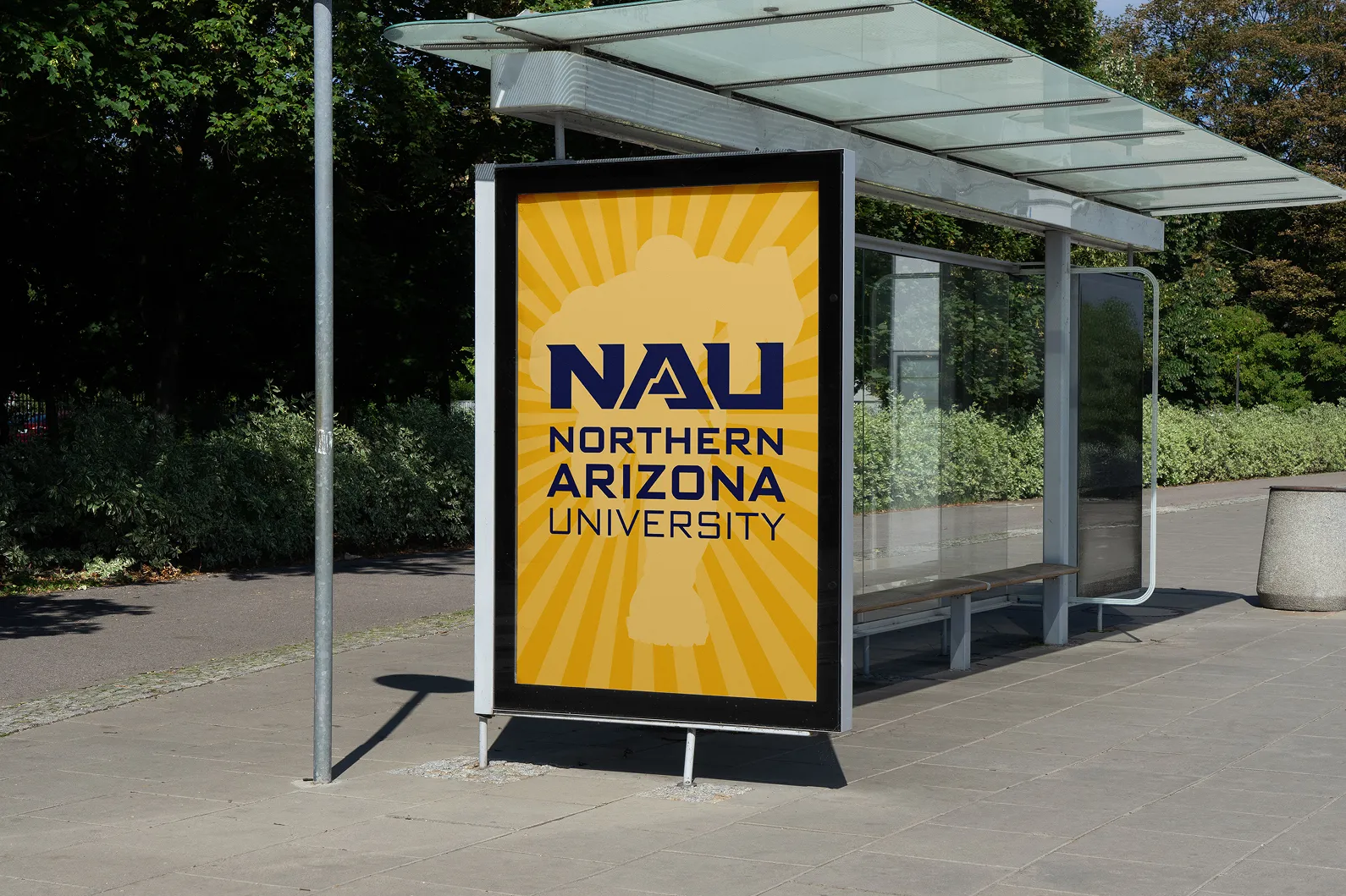 An NAU poster displayed in a bus shelter beside a campus path.