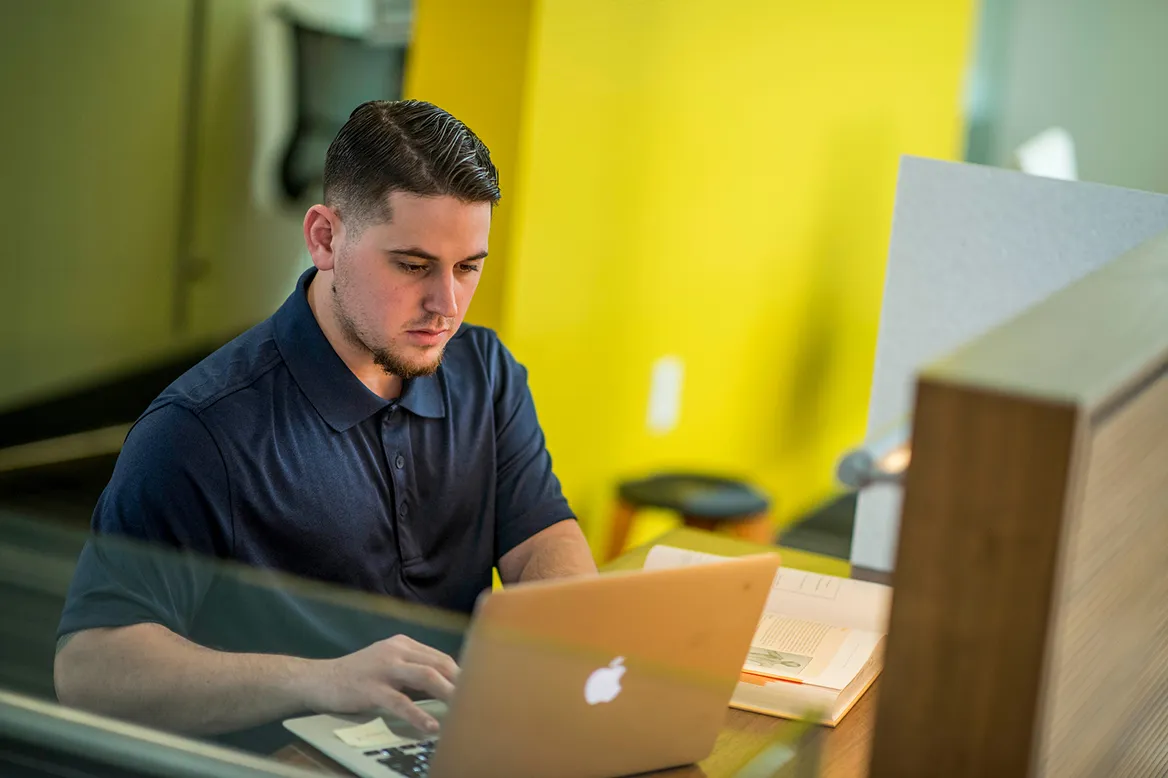 A student working on a laptop in a campus study space.