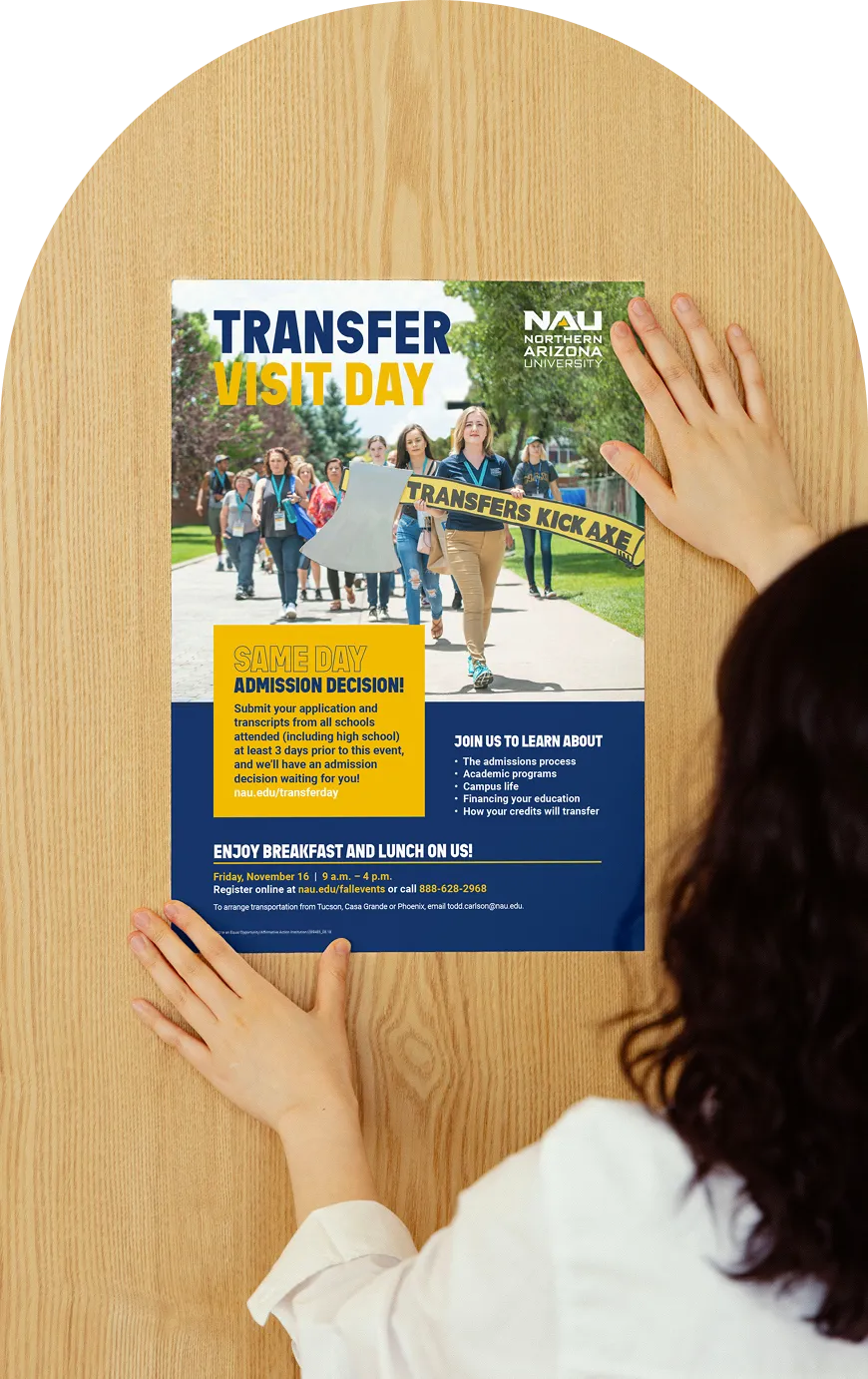 Hands placing an NAU Transfer Visit Day poster on a wooden board.