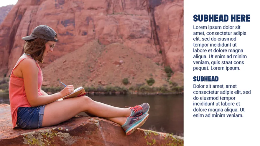Woman wearing cap and glasses writing in journal while sitting on rock by river with cliffs behind.