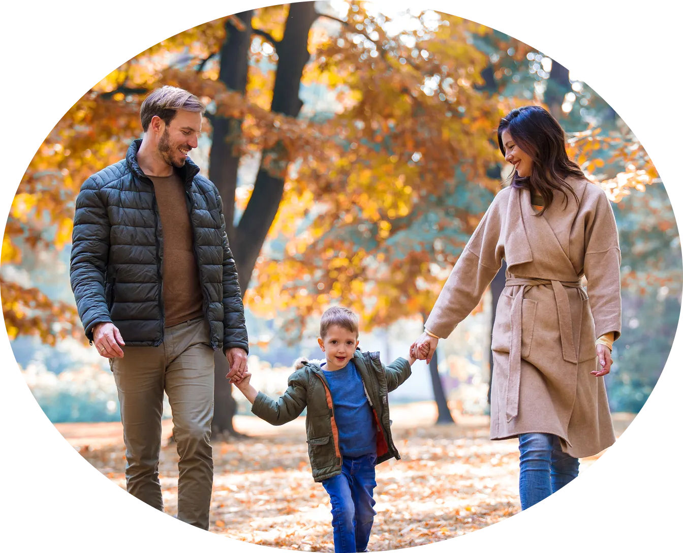 A family walking together through autumn leaves, holding a child's hands.