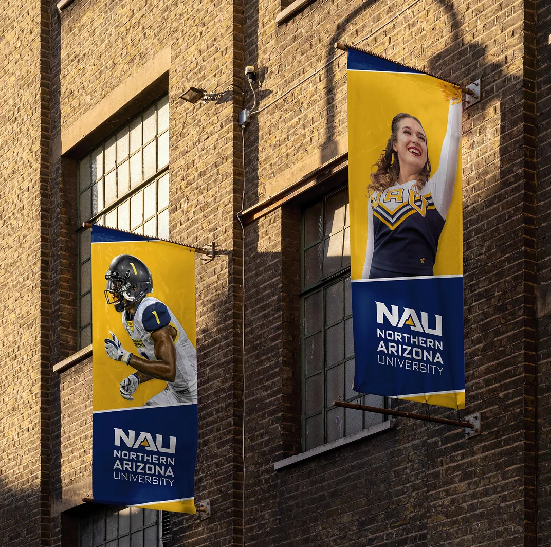 NAU athletics banners on a brick building showing a footballer and a cheerleader.