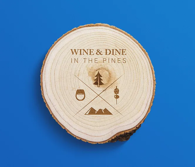 A wood slice engraved "Wine & Dine in the Pines" on a blue background.