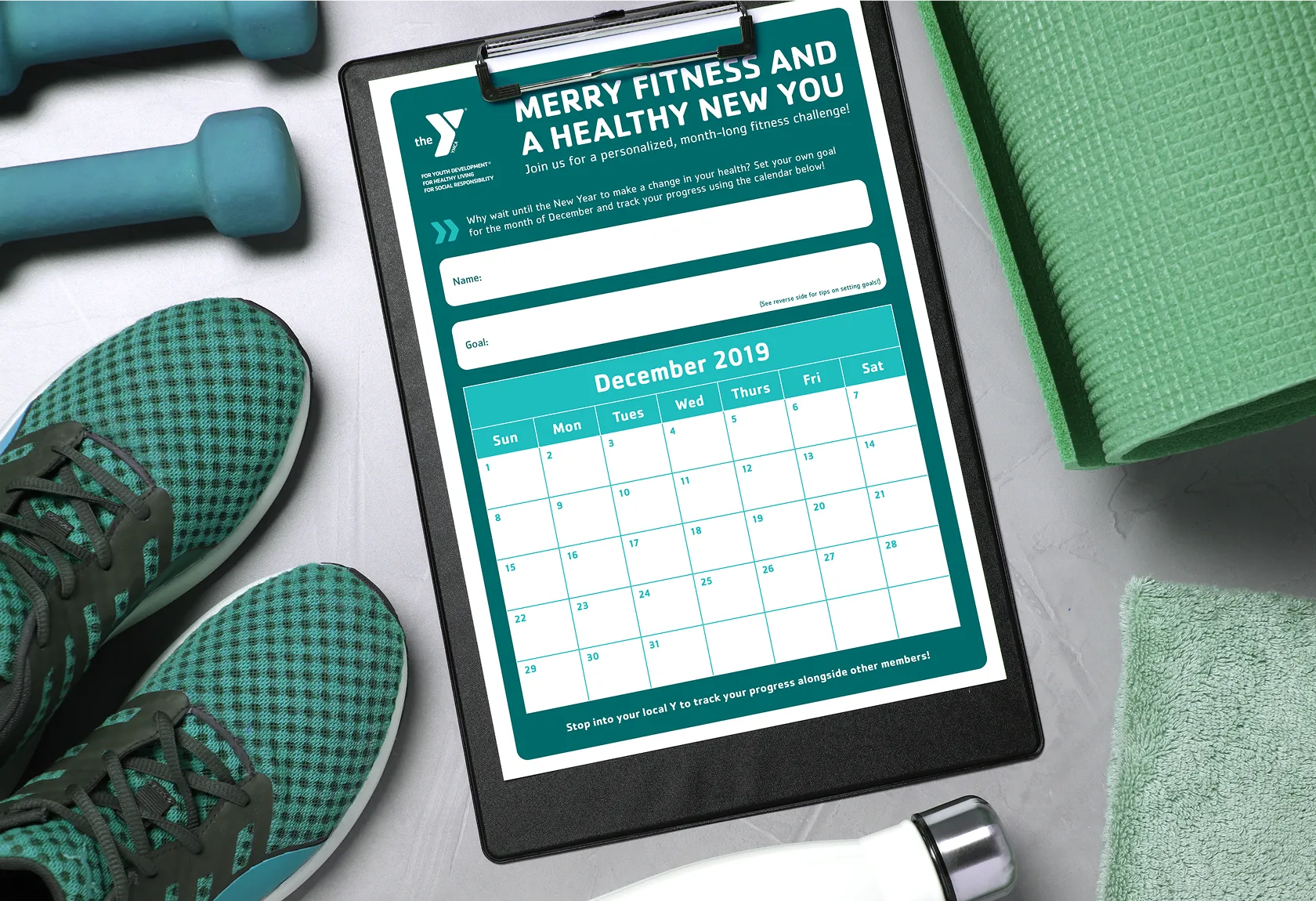 A tablet showing a YMCA "Merry fitness and a healthy new year" calendar beside gym equipment.