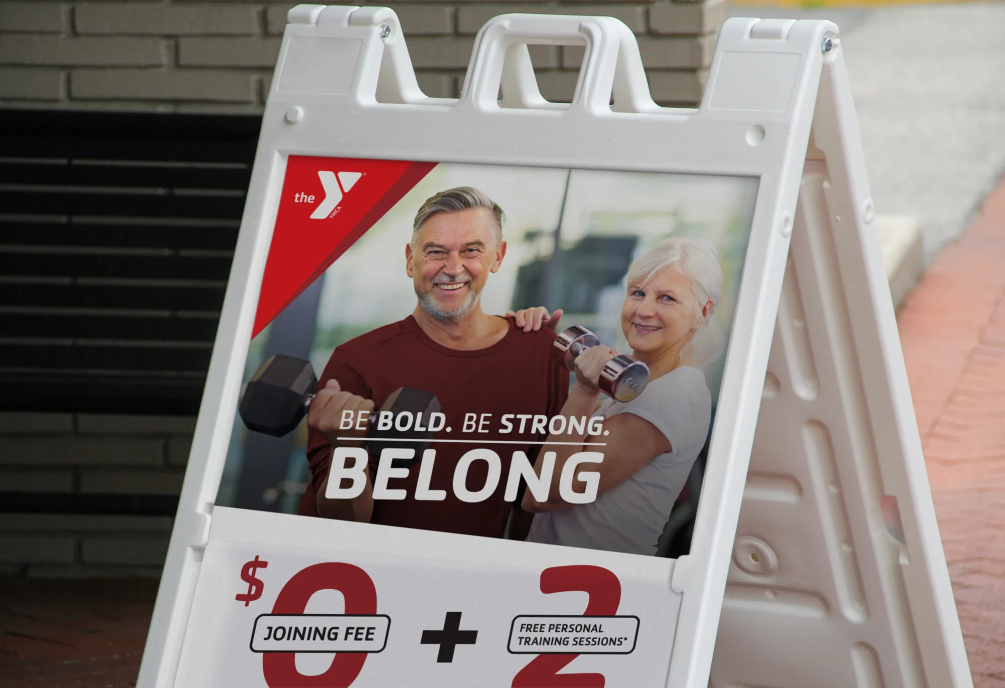 A YMCA "Be Bold. Be Strong. Belong." A-frame sign advertising a $0 joining fee.