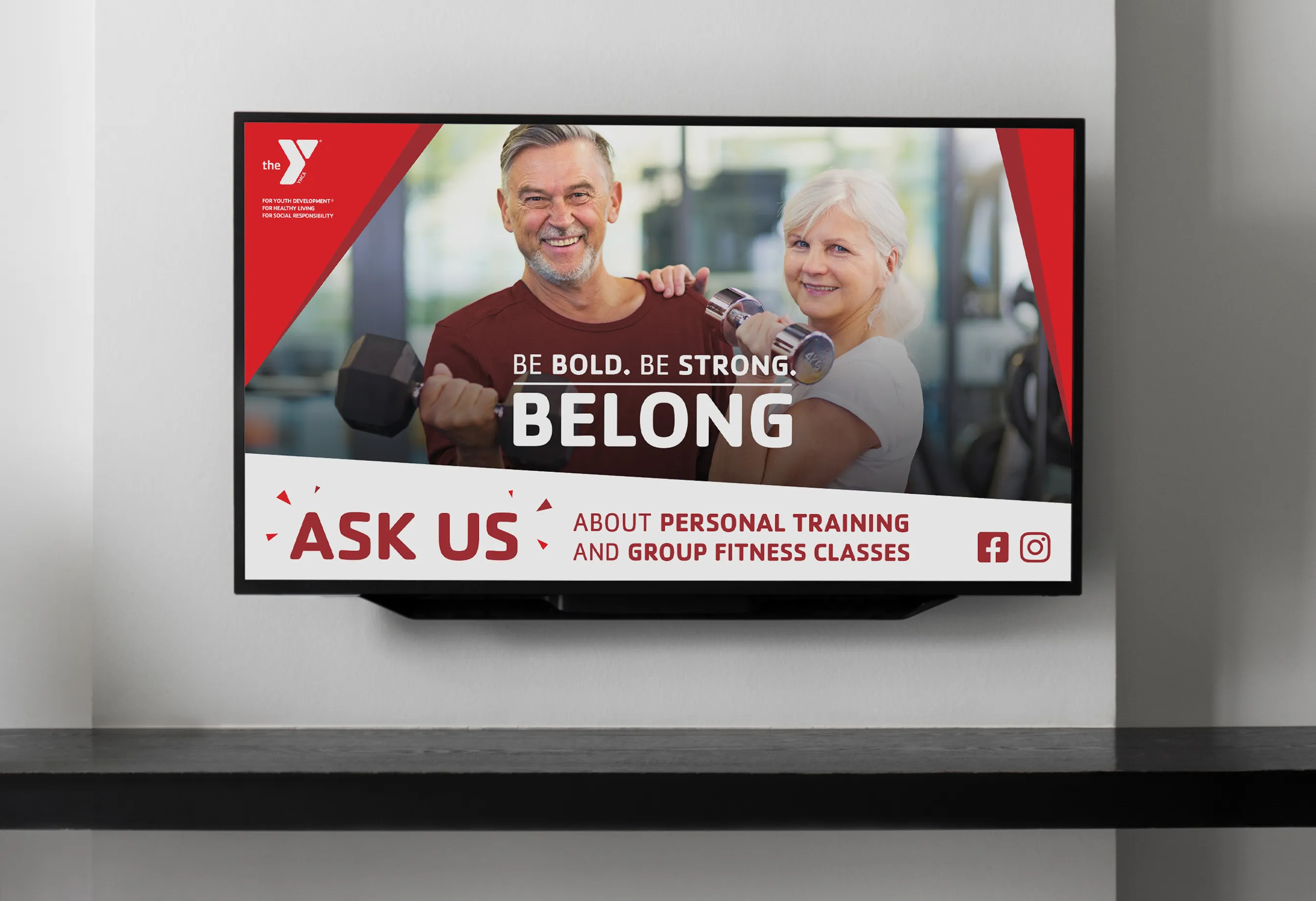 A wall-mounted screen showing a YMCA "Belong" advert inviting members to ask about training.