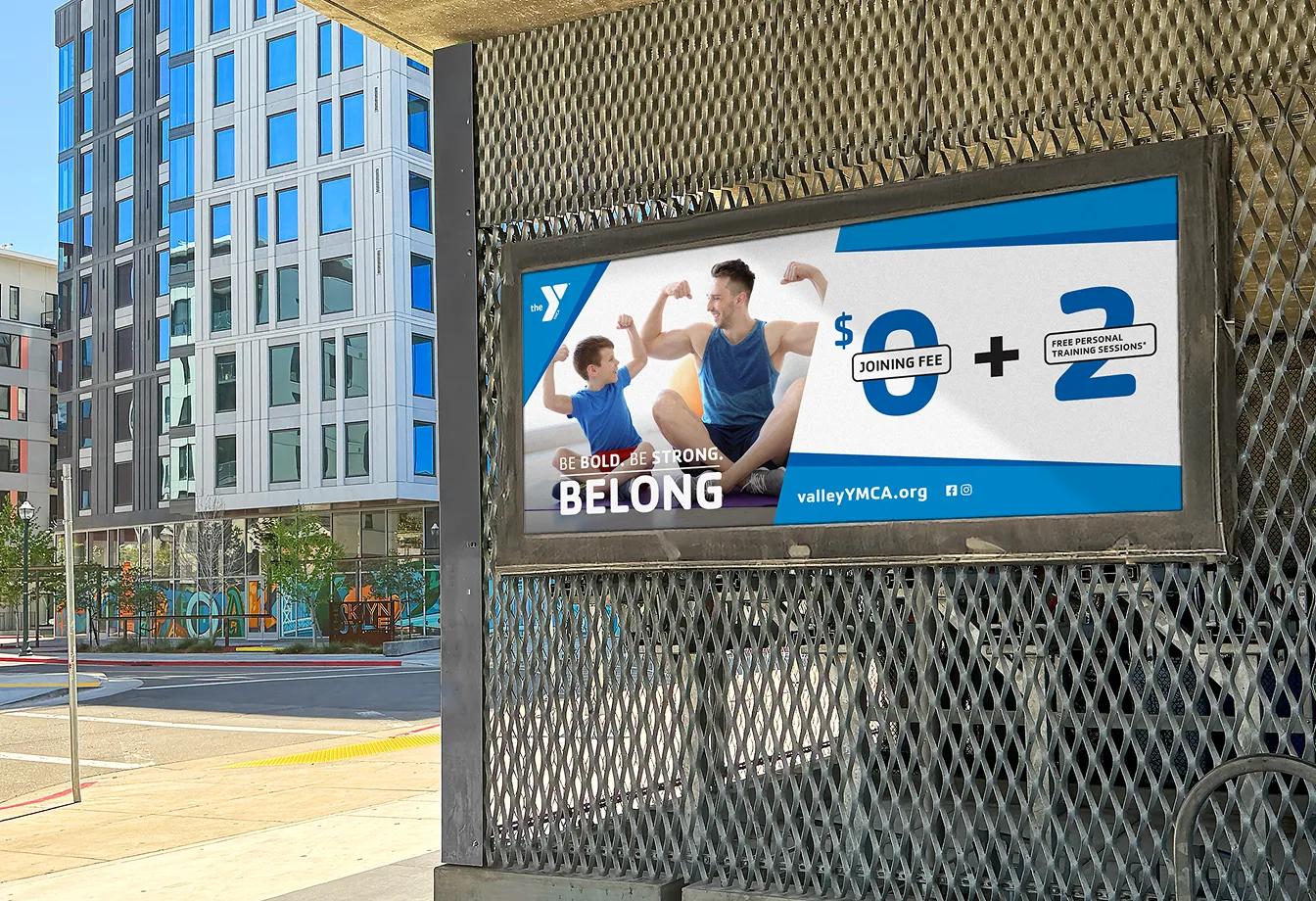 A YMCA "Belong" advert displayed on a transit shelter screen.