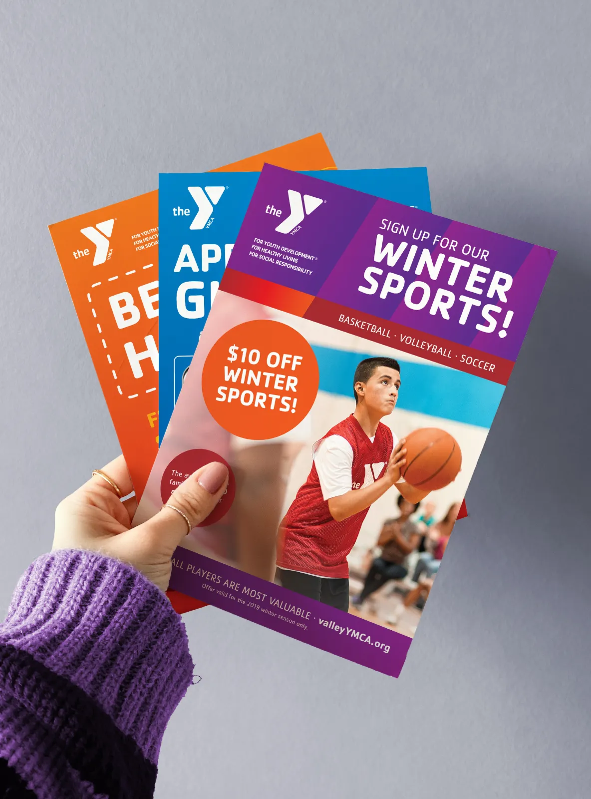 A hand holding a fan of YMCA winter sports and programme flyers.