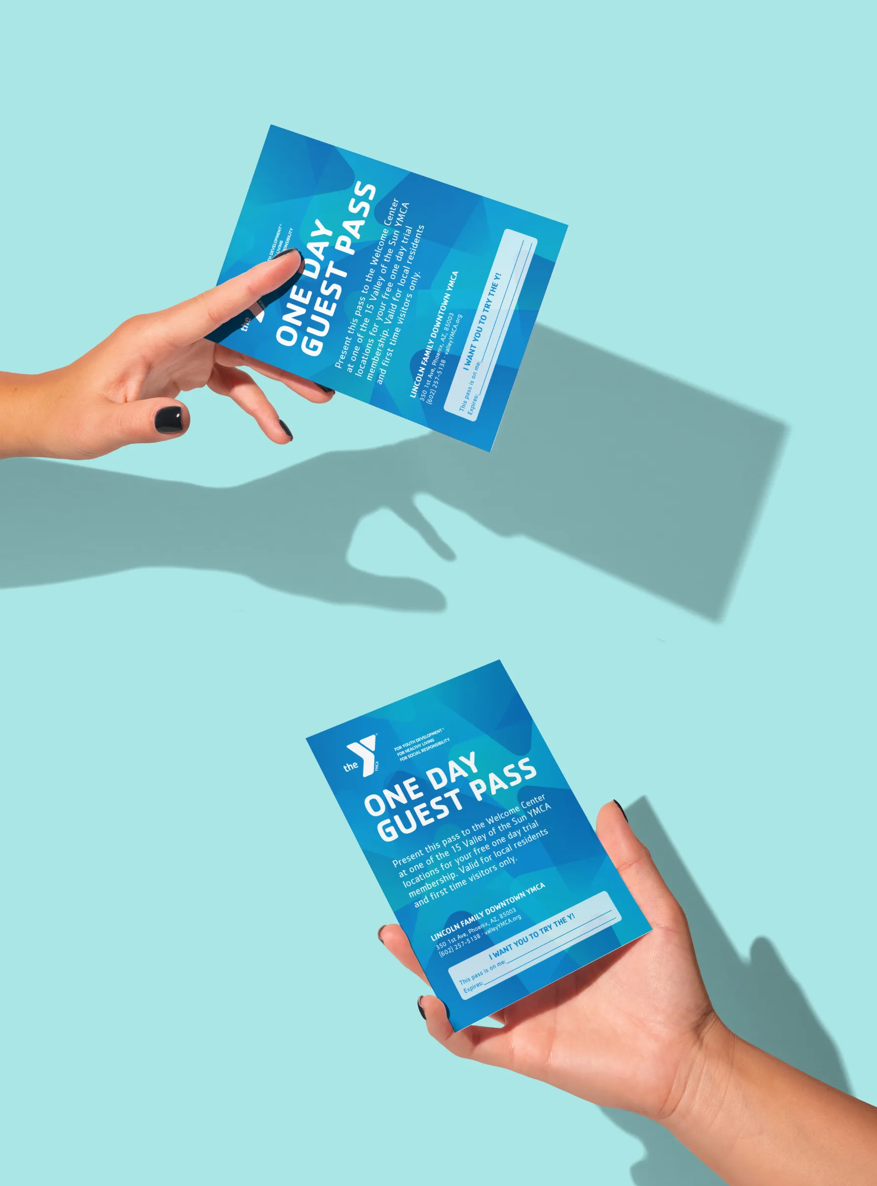 Hands holding YMCA one-day guest passes against a pale blue background.