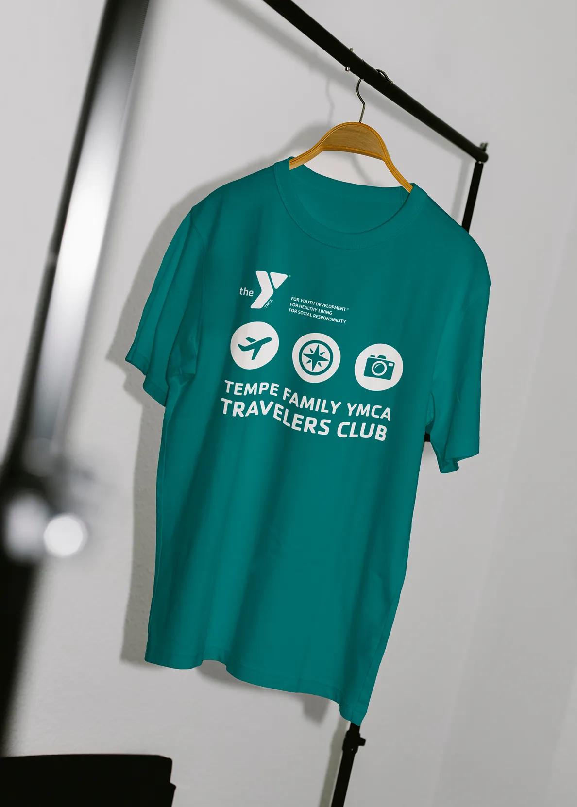 A teal YMCA "Tempe Family YMCA Travelers Club" t-shirt on a hanger.