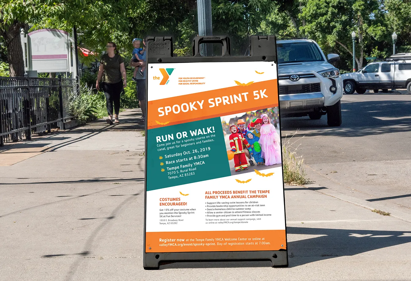 A Spooky Sprint 5K A-frame sign on a pavement outside a YMCA branch.