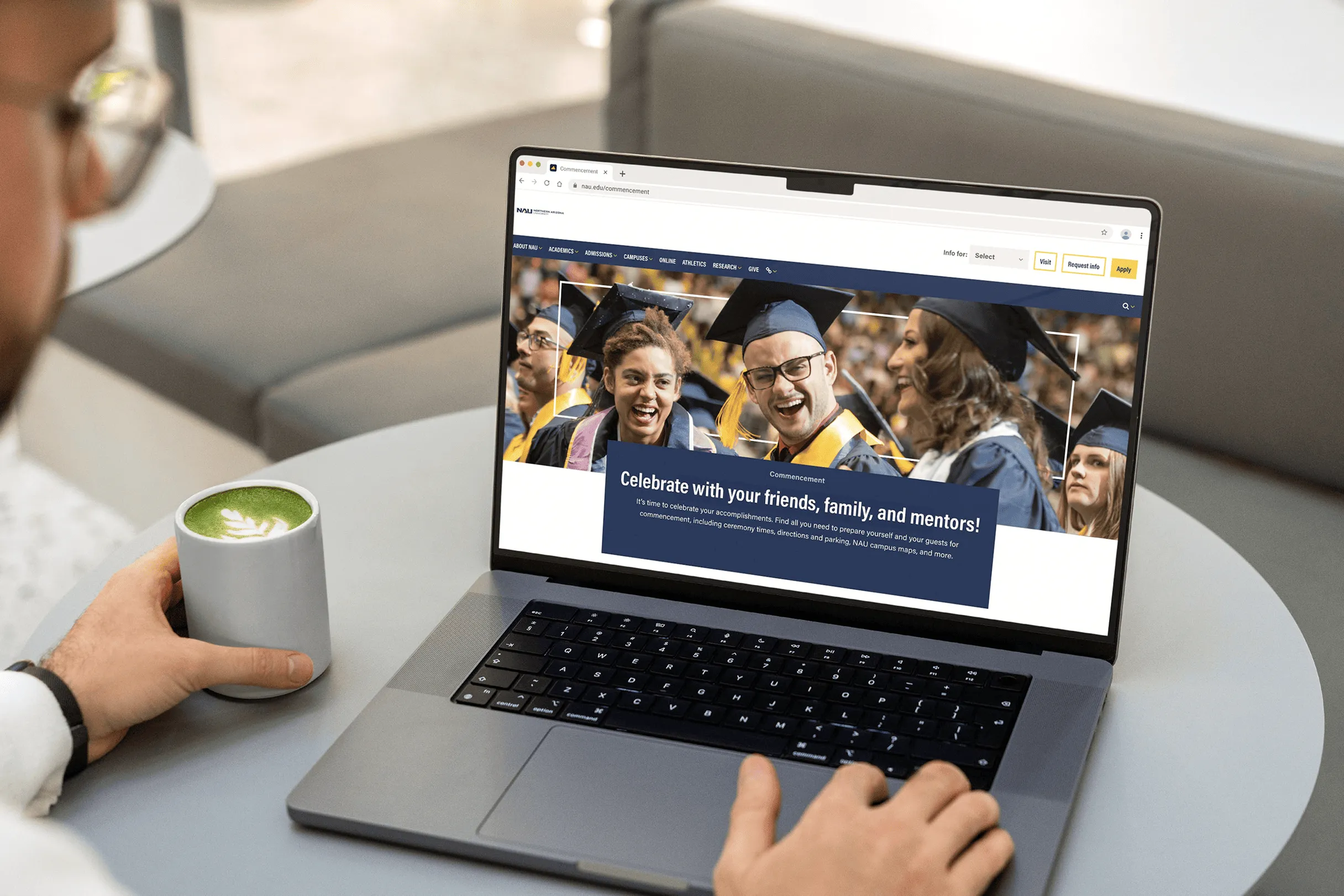 A person with a green latte viewing the NAU commencement page on a laptop.
